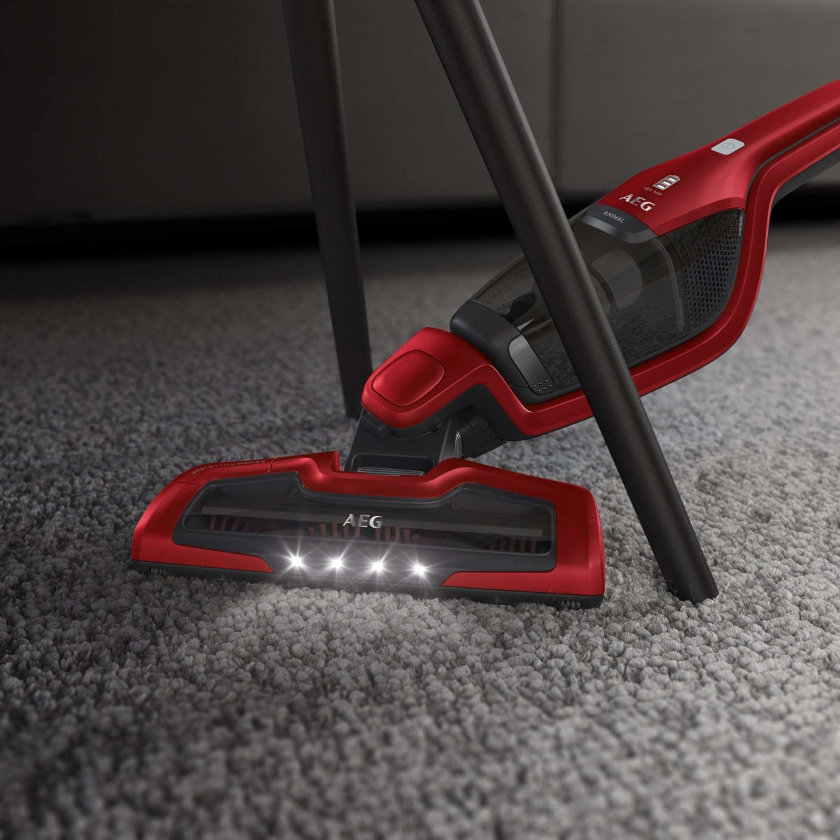 Aspiradora AEG roja con LED limpiando alfombra bajo mueble