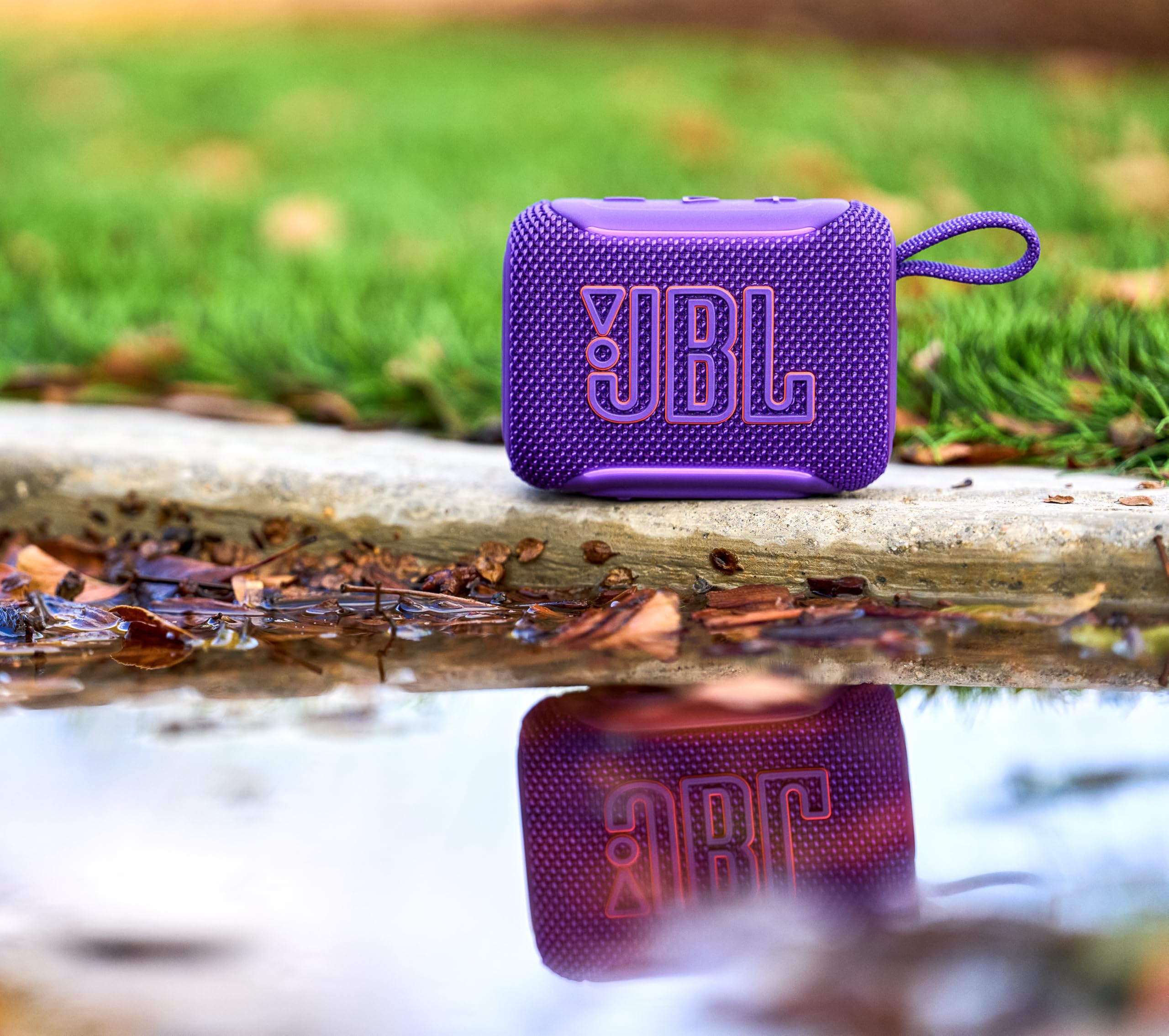 Altavoz Bluetooth JBL Go 5 púrpura sobre piedra mojada con reflejo en charco