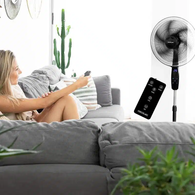 Mujer controlando ventilador de pie Cecotec con mando a distancia digital en salón.