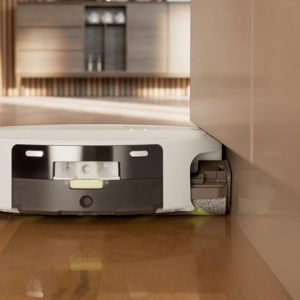 Robot aspirador con mopa limpiando bordes junto a mueble de cocina sobre suelo de madera