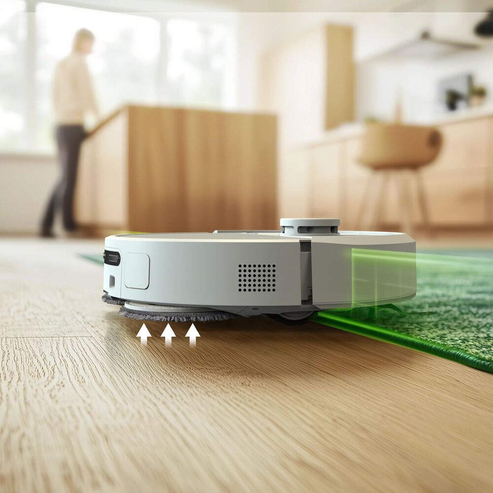 Robot aspirador inteligente con sensores láser limpiando el borde de una alfombra sobre suelo de madera