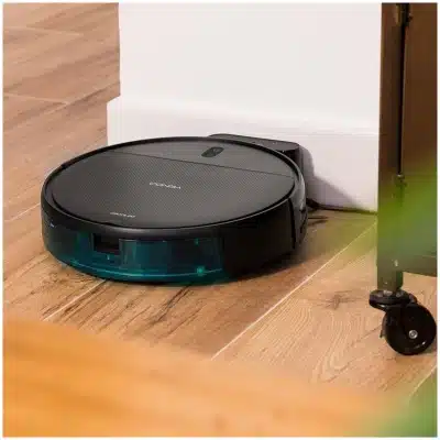 Robot aspirador Cecotec Conga negro con detalle verde, recargando o navegando junto a mueble sobre parquet