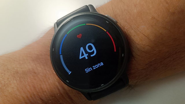 Reloj inteligente negro en muñeca mostrando medición de ritmo cardíaco 49 lpm con zonas de color.