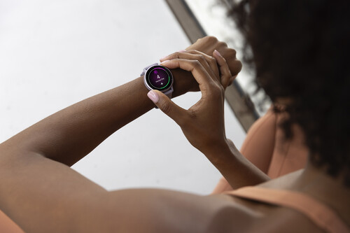 Mujer usando smartwatch redondo negro con pantalla táctil mientras lo opera con el dedo.