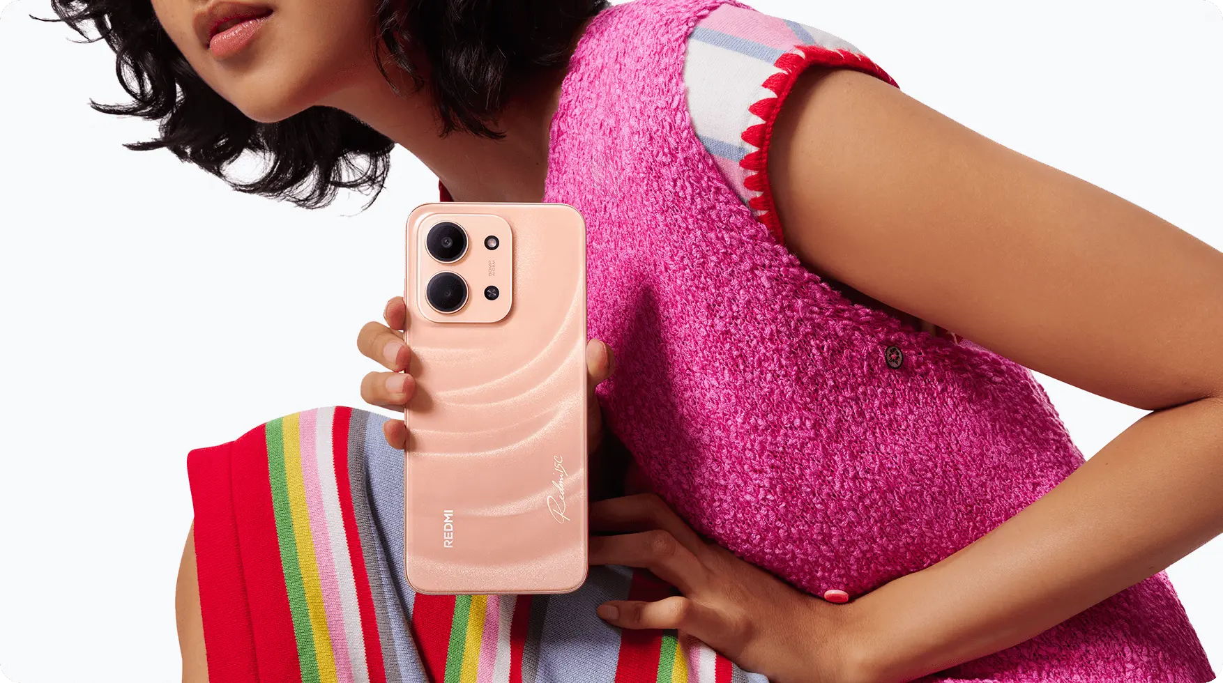 Mujer sosteniendo un smartphone Redmi en color melocotón mostrando su trasera con doble cámara y diseño ondulado