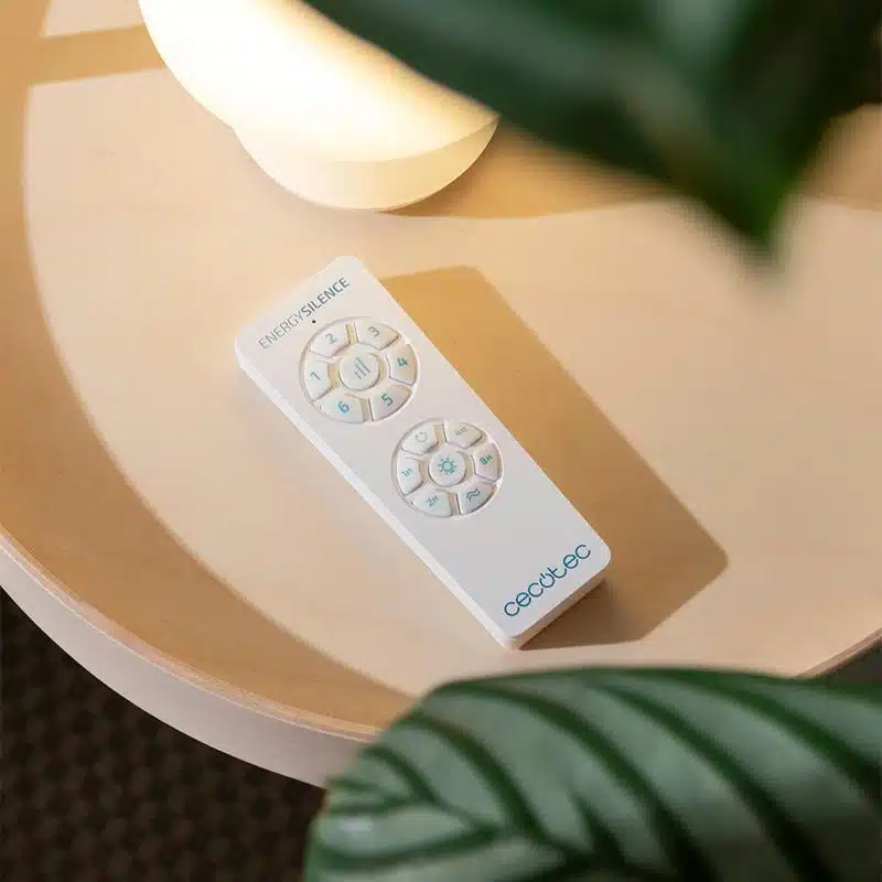 Mando a distancia Cecotec EnergySilence blanco sobre mesa de madera con planta verde decorativa