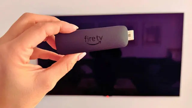 Dispositivo Fire TV en mano frente a televisor