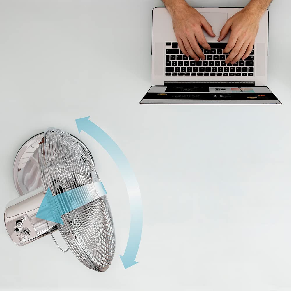 Ventilador sobremesa cromado oscilante junto a portátil en fondo blanco.