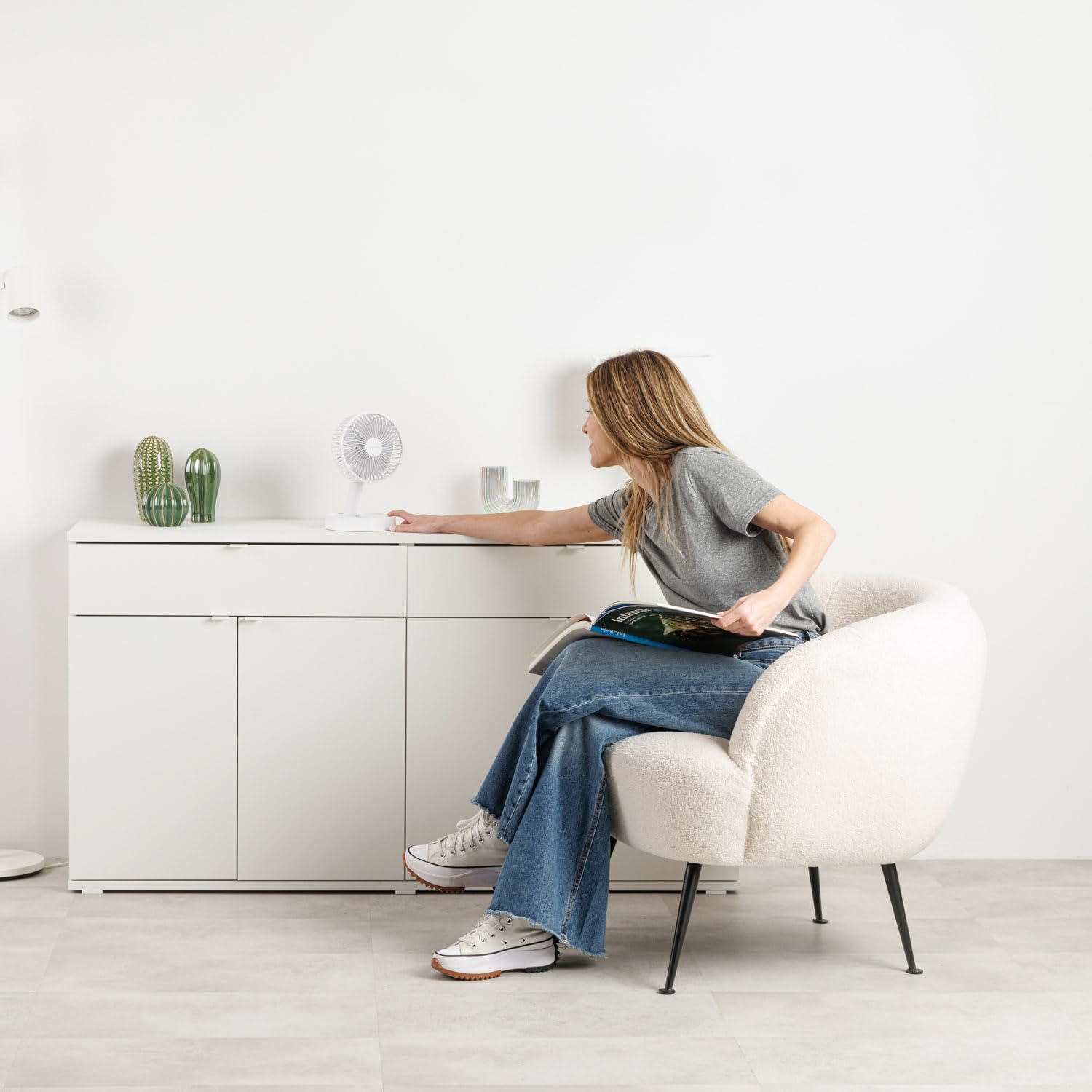 Mujer usando ventilador portátil plegable blanco en sala minimalista.