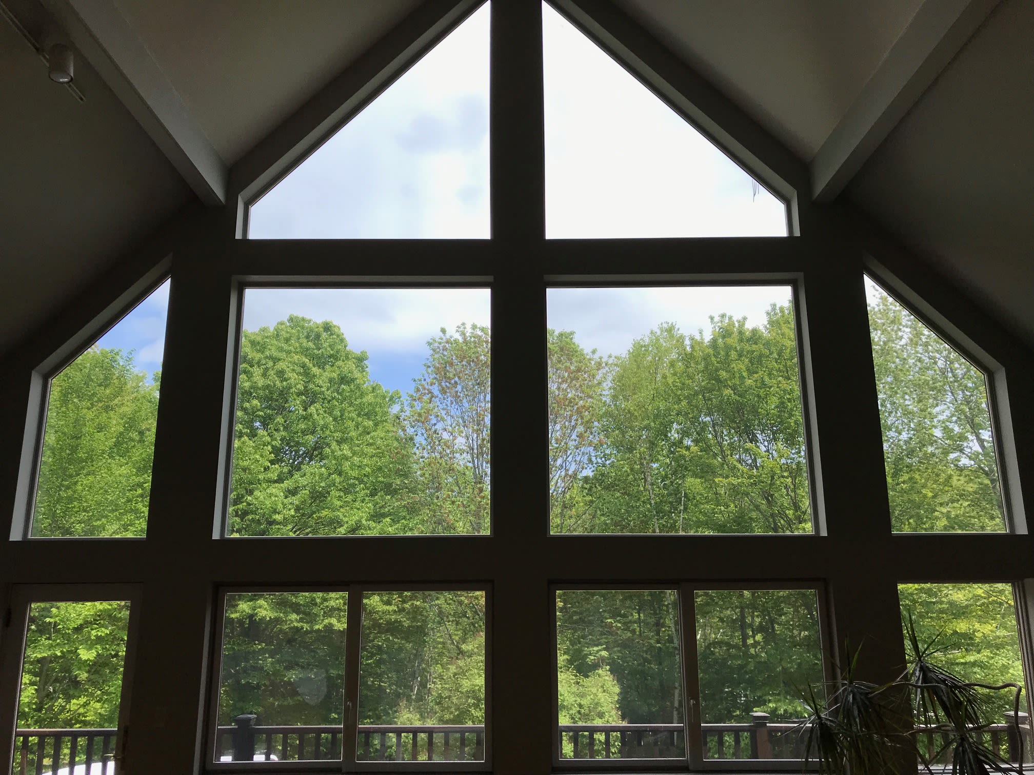 Vaulted gable wall of tinted windows over wooded deck