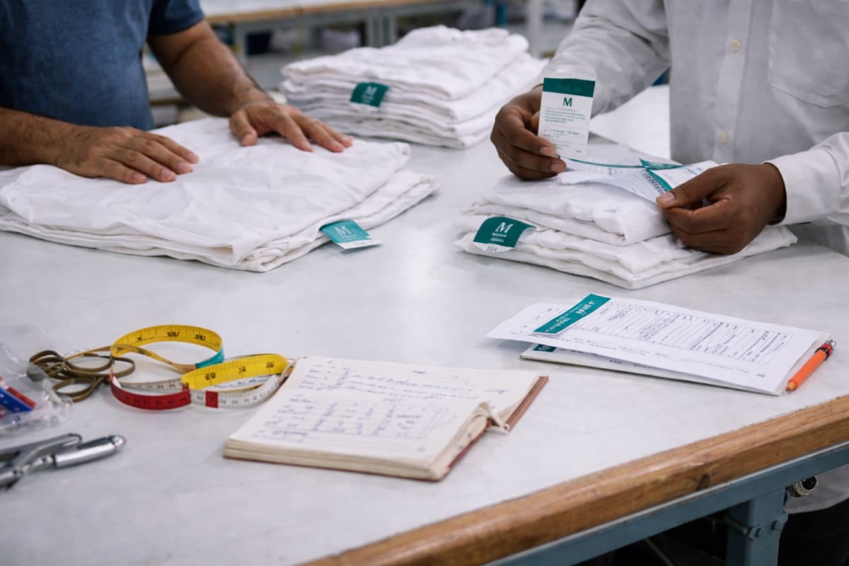 Inspectors measuring and checking white t-shirts against a spec sheet