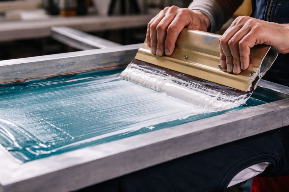 Hands pulling a squeegee across a screen printing frame