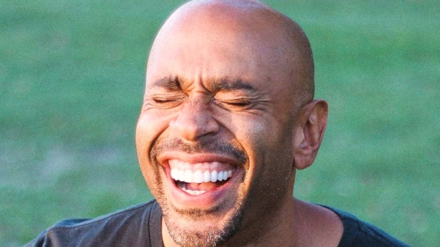 Chibs Okereke — Man laughing against blurred green background