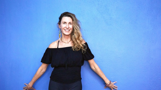 Janet — Woman smiling with arms extended against blue background