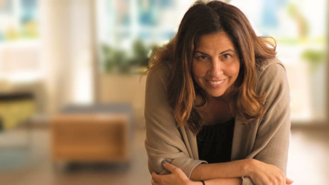 Manal - Mattain — Woman in beige cardigan indoors smiling