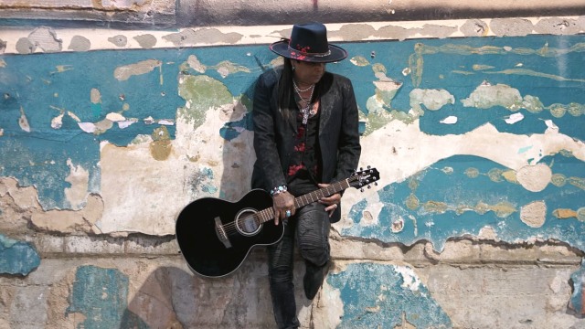 Micki Free — Musician with acoustic guitar against mural
