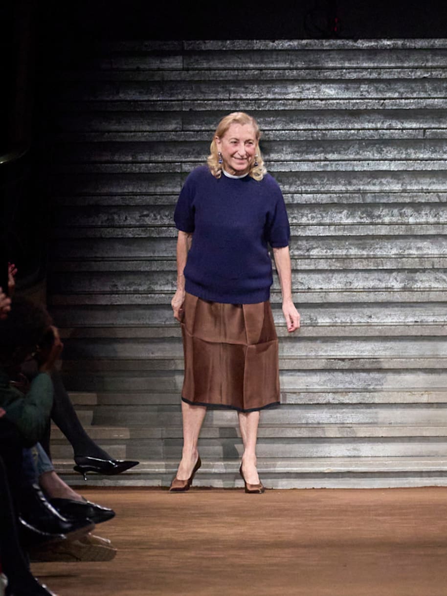Prada Miuccia Prada Miu Miu Fashionweek Runway Frau mit blonden Haaren, dunkles Top und brauner Rock