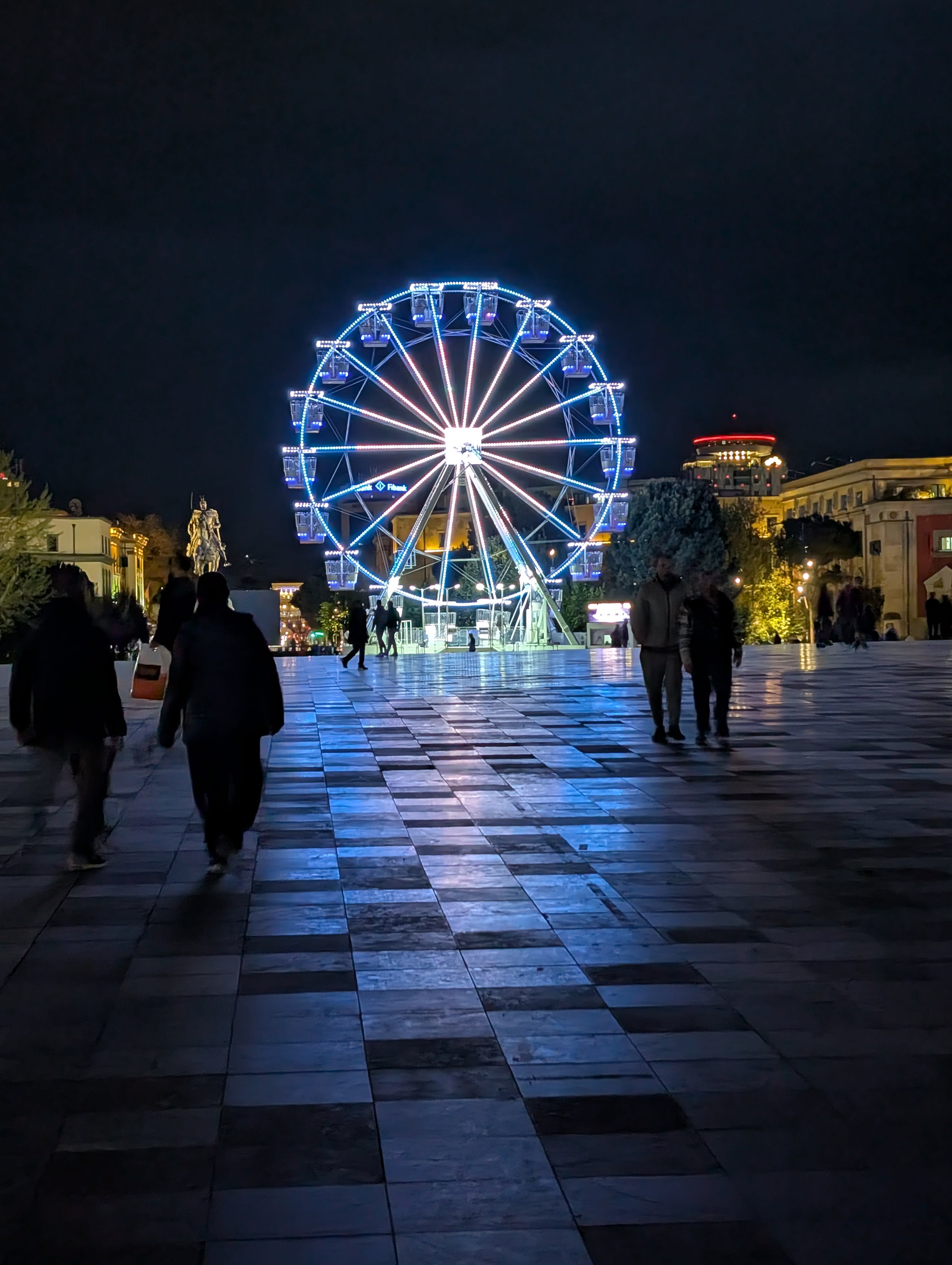 A Ferris wheel lights up Skanderbeg Square in Tirana at night.
