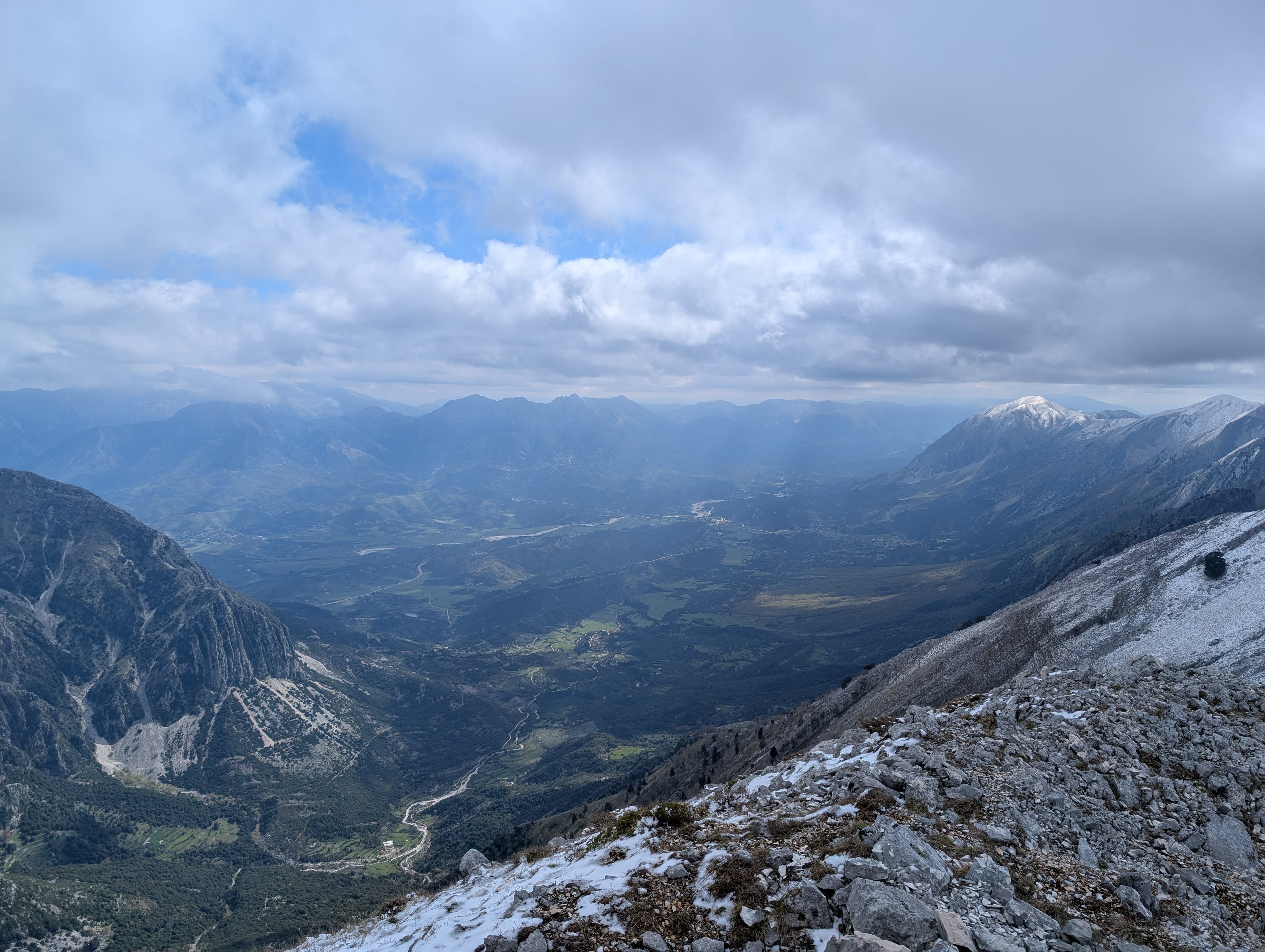 View looking Southeast from the Peak of Maja Paliskës. A large valley with light shining down between clouds.