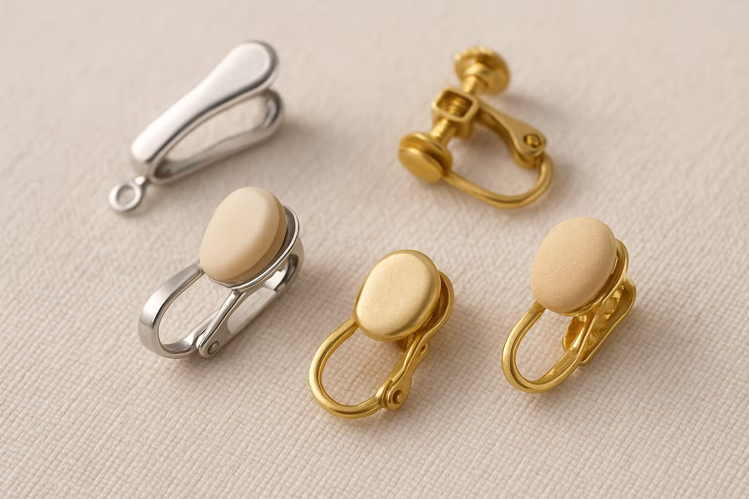 Gros plan sur plusieurs boucles d'oreilles clip disposées sur un tissu neutre: clips métalliques, coussinets en silicone, modèles à vis, textures détaillées