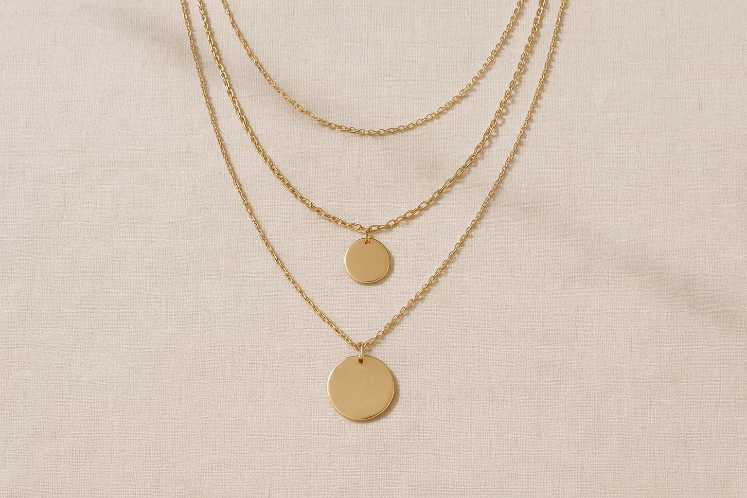 Plusieurs colliers superposés posés sur lin, montrant différentes longueurs, textures et pendentifs