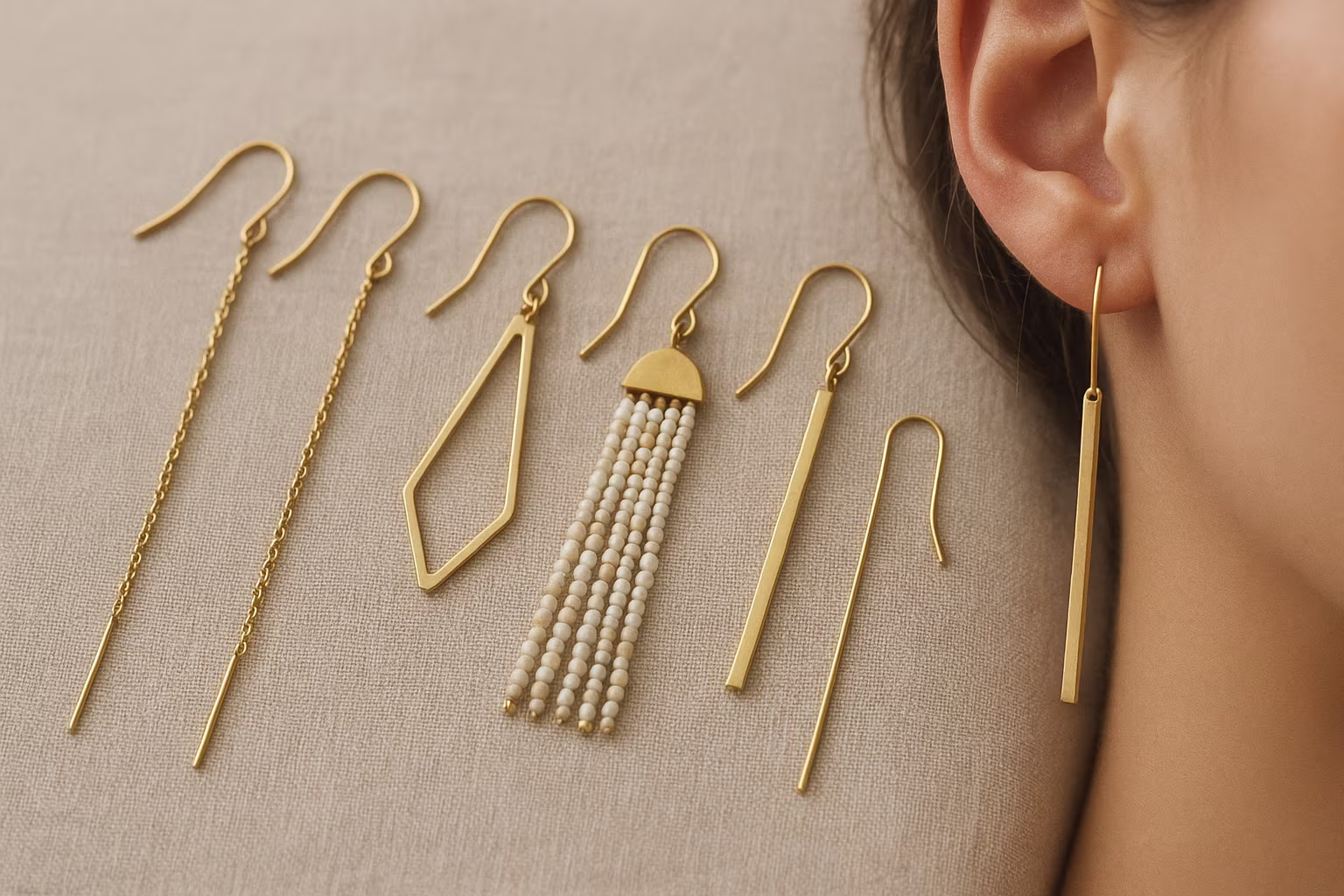 Collection de boucles d'oreilles longues variées sur tissu neutre montrant chaînes, pompons et barres métalliques