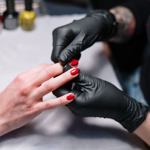 Técnica con guantes trabajando un esmaltado rojo en el salón