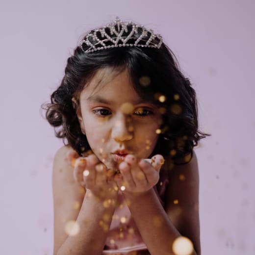 Niña con tiara soplando glitter, glitter facial y perlas adhesivas