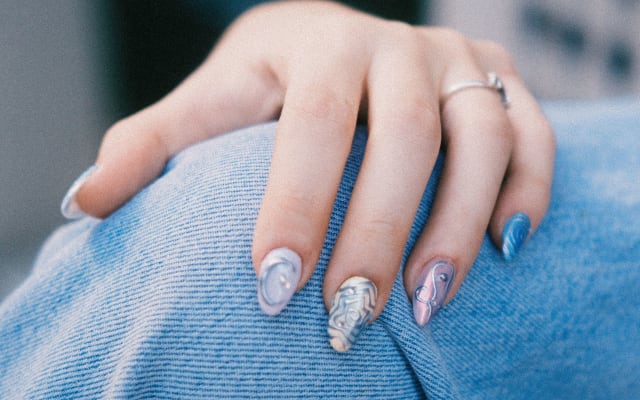 Manicura en tonos nude con destellos, sobre un suéter azul