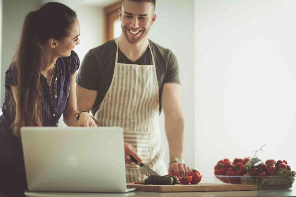 Smiling chef in black uniform cooking colorful vegetables in pan