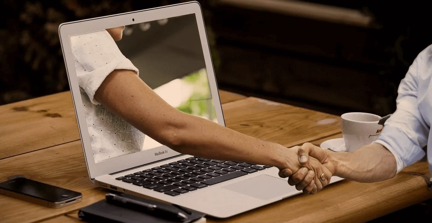 Two people shaking hands through laptop screen in virtual business meeting