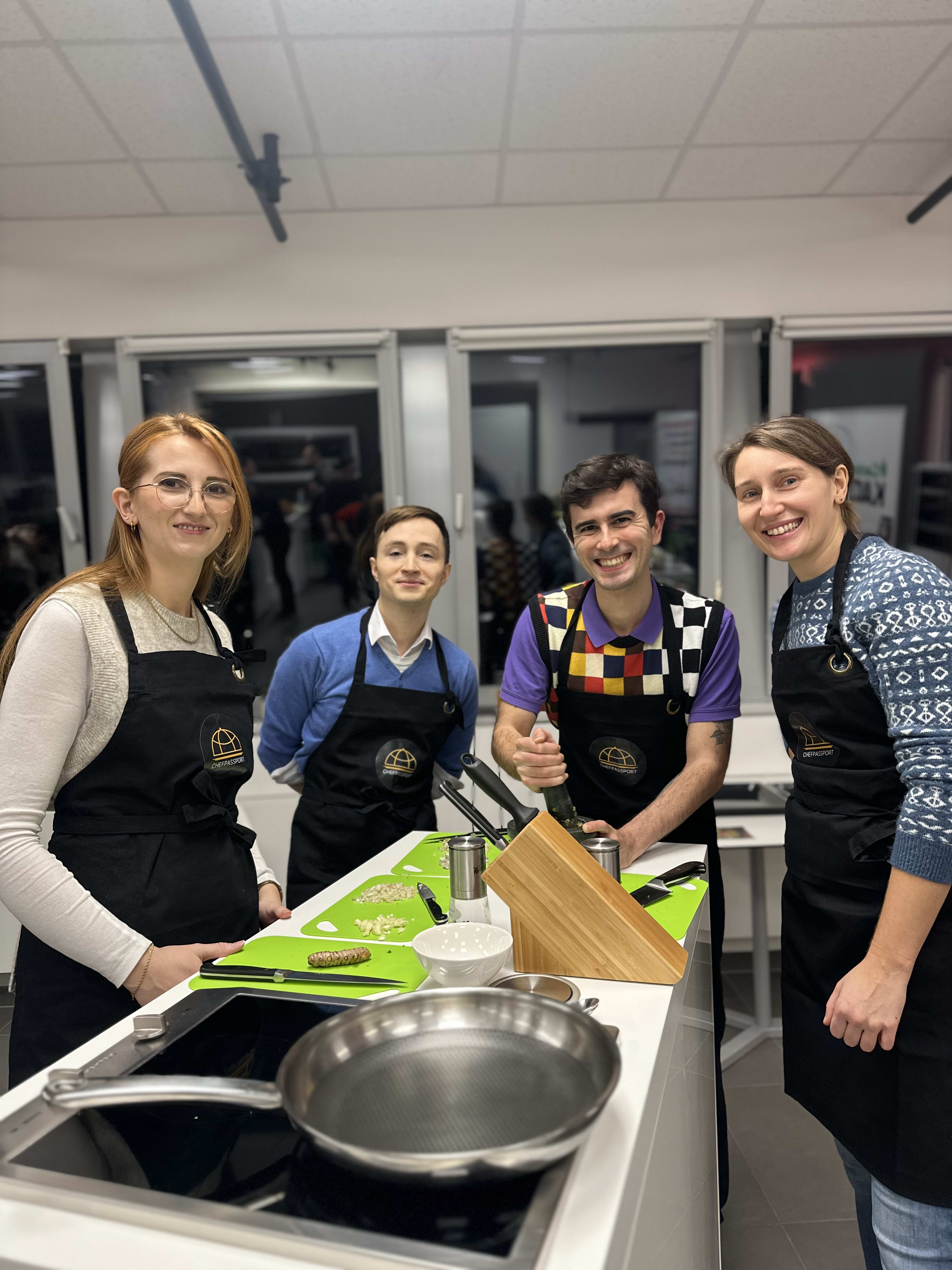 Four people wearing black aprons standing together in a cooking class kitchen