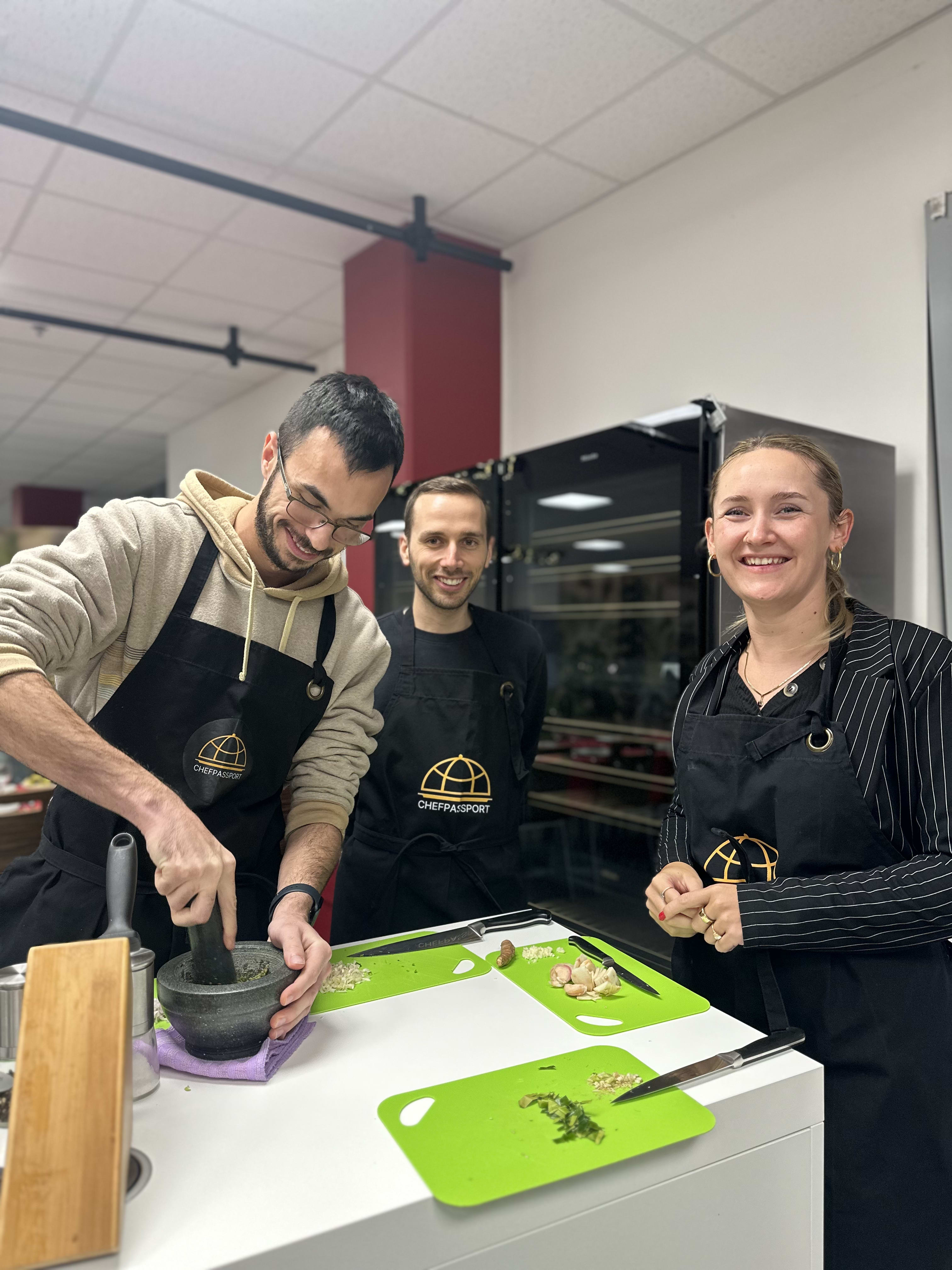 Three people wearing Chefpassport aprons preparing food together in a commercial kitchen