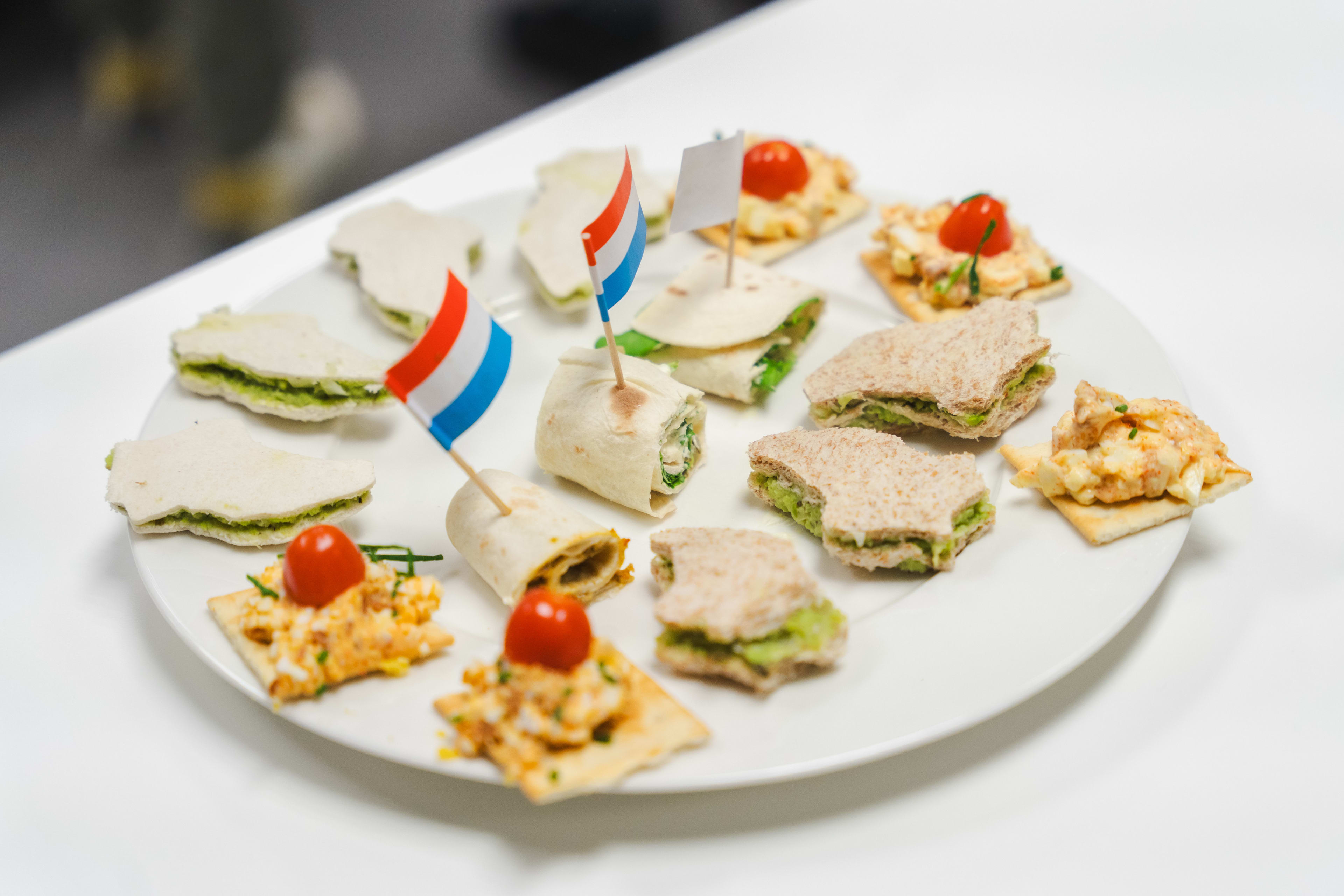 Platter of assorted finger sandwiches, wraps, and crackers with cherry tomatoes and decorative flags