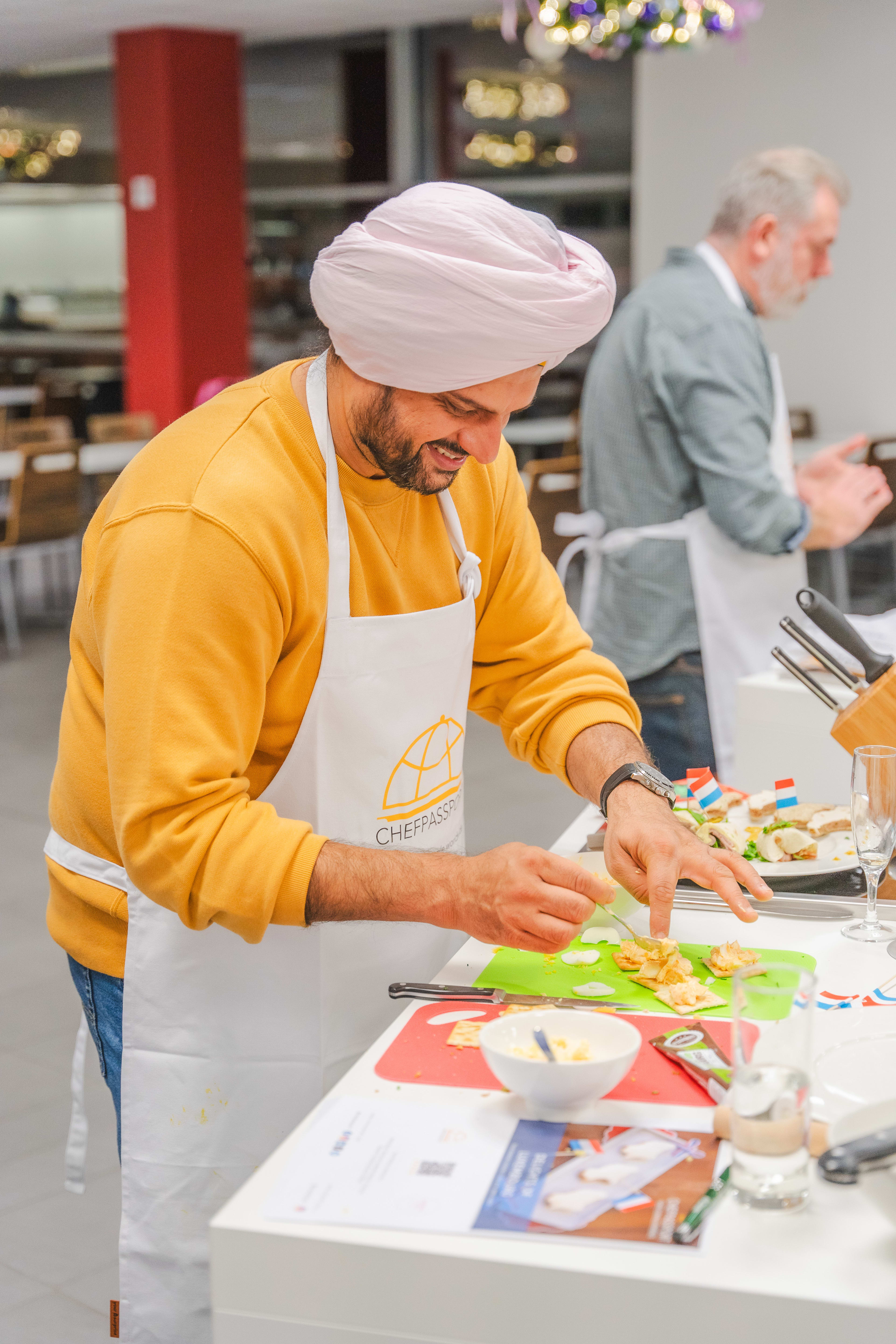 Man in white turban and yellow sweatshirt preparing food on green cutting board in kitchen