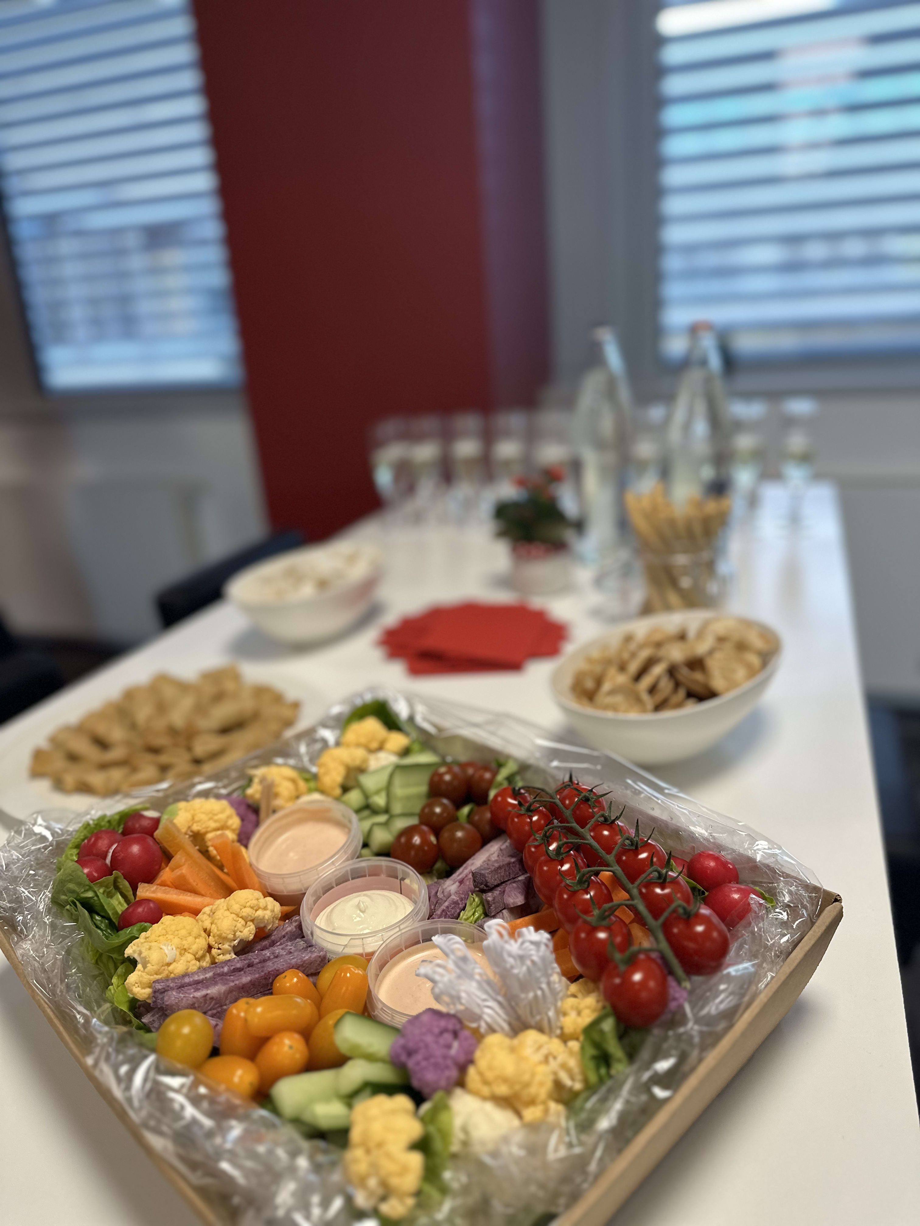 Colorful vegetable platter with dips and snacks arranged on white table for office meeting