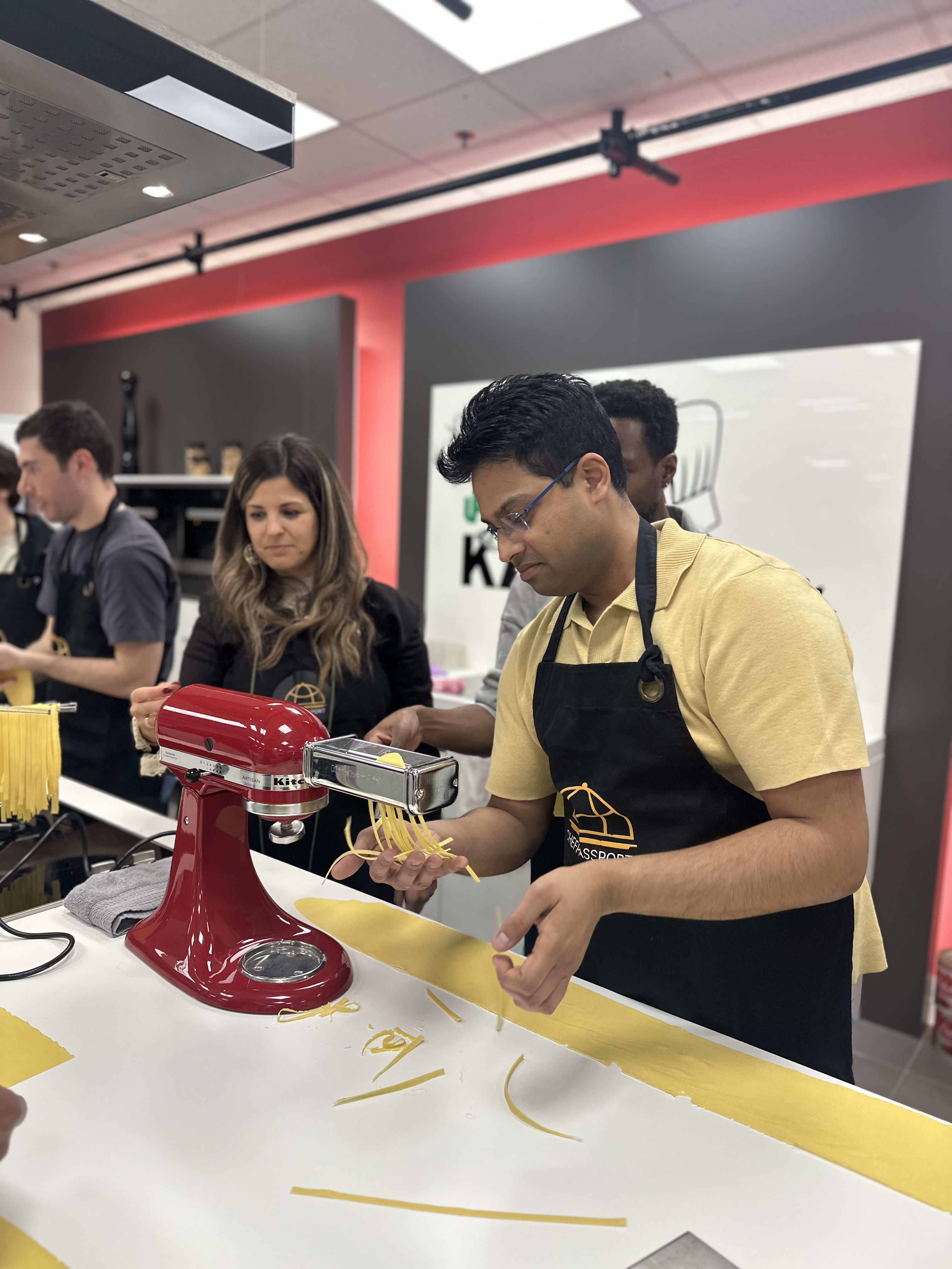 Man in yellow shirt using red stand mixer to make fresh pasta in cooking class