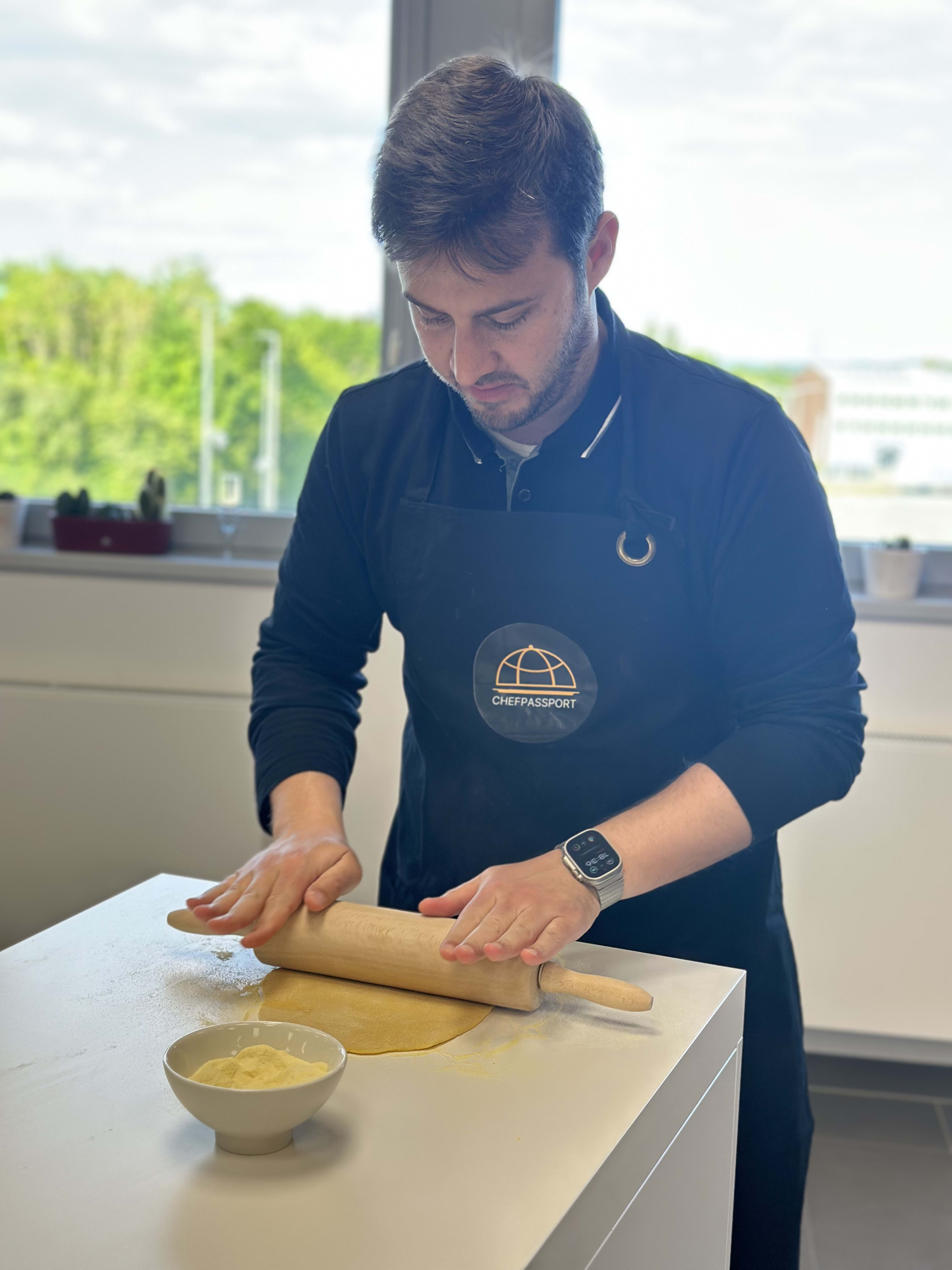 Man in navy ChefPassport polo shirt rolling dough with wooden rolling pin in kitchen