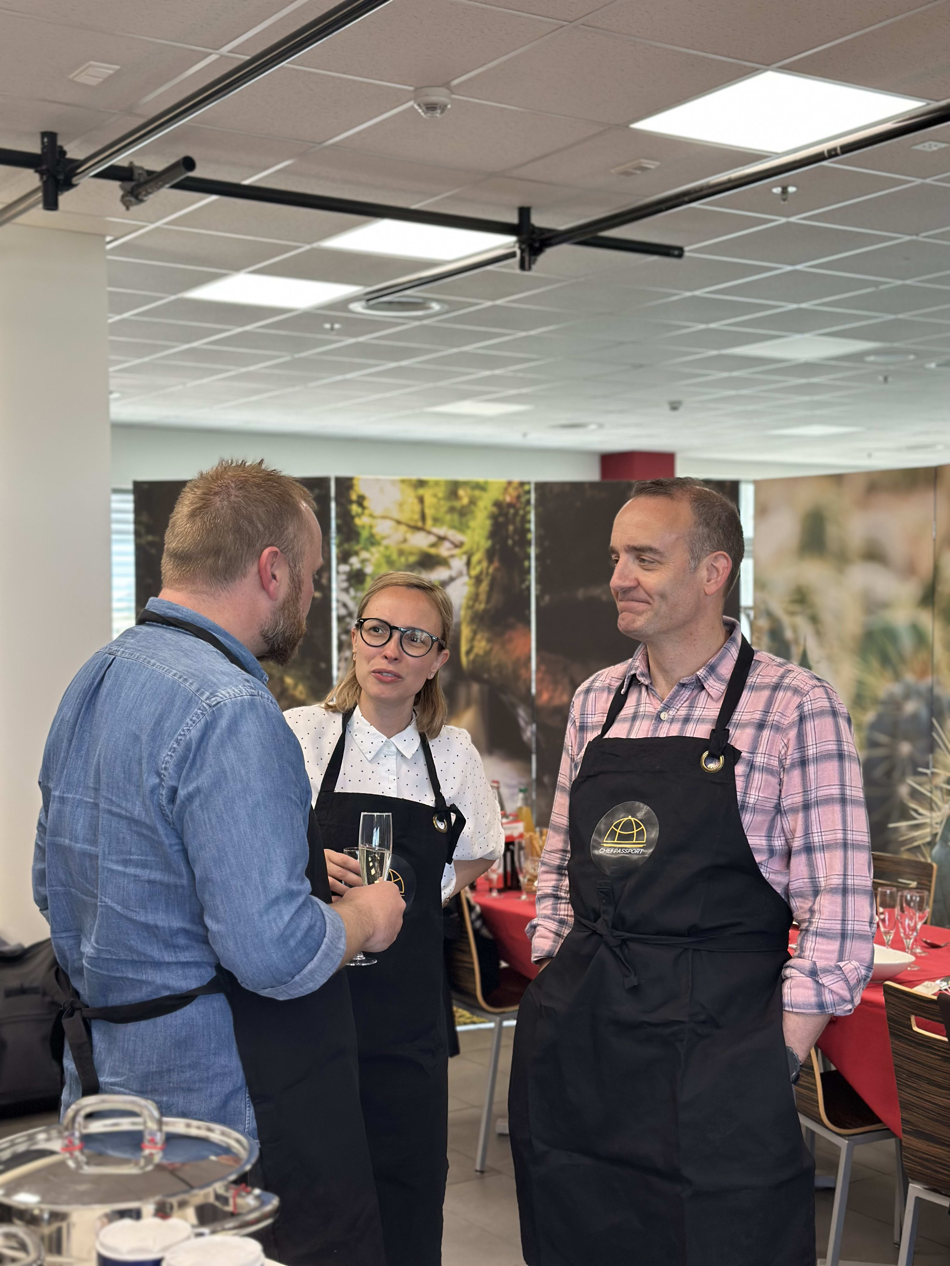 Three people in black aprons conversing at a corporate event with champagne glasses