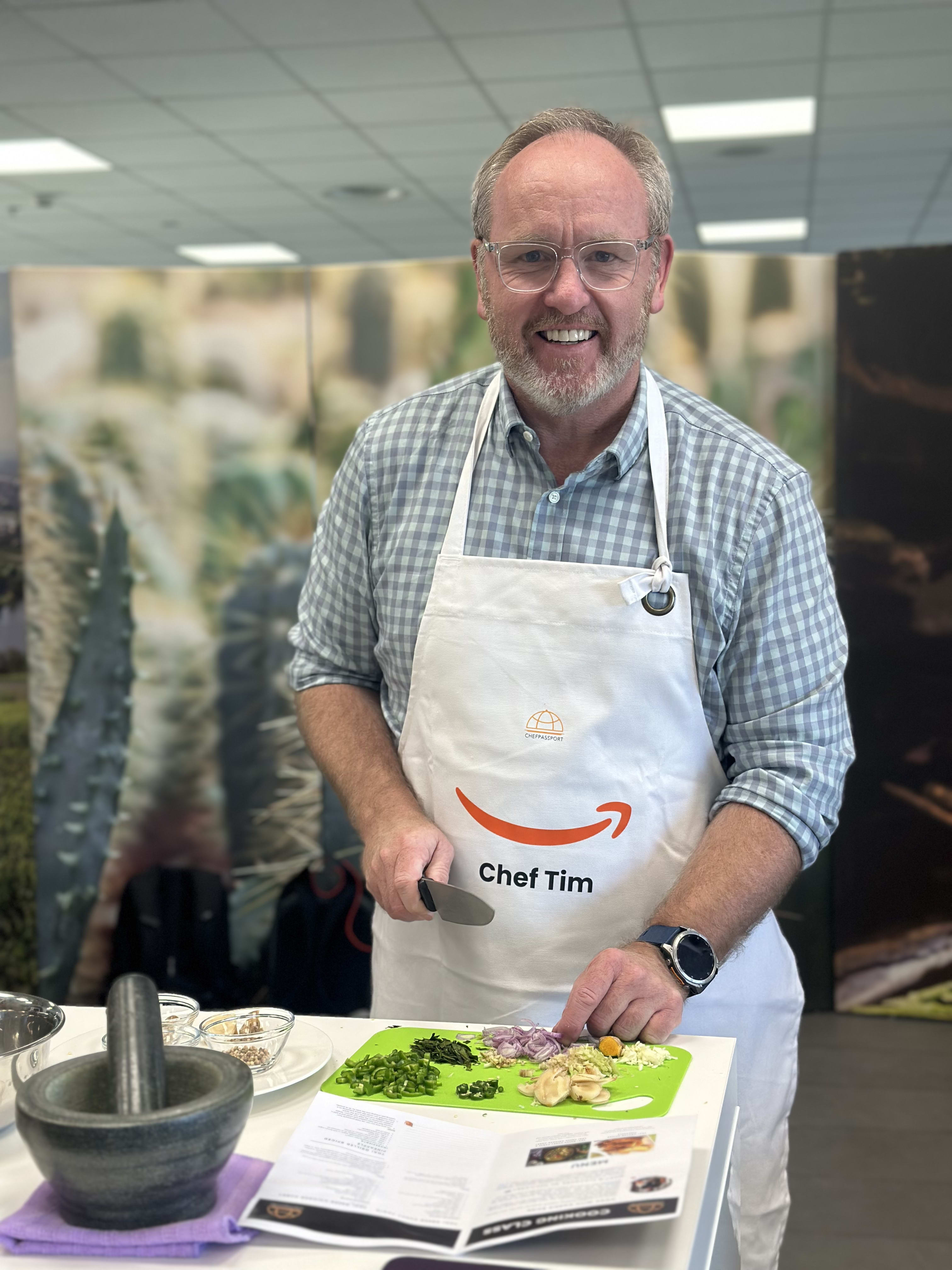 Man in apron labeled Chef Tim preparing food ingredients at cooking demonstration in office kitchen