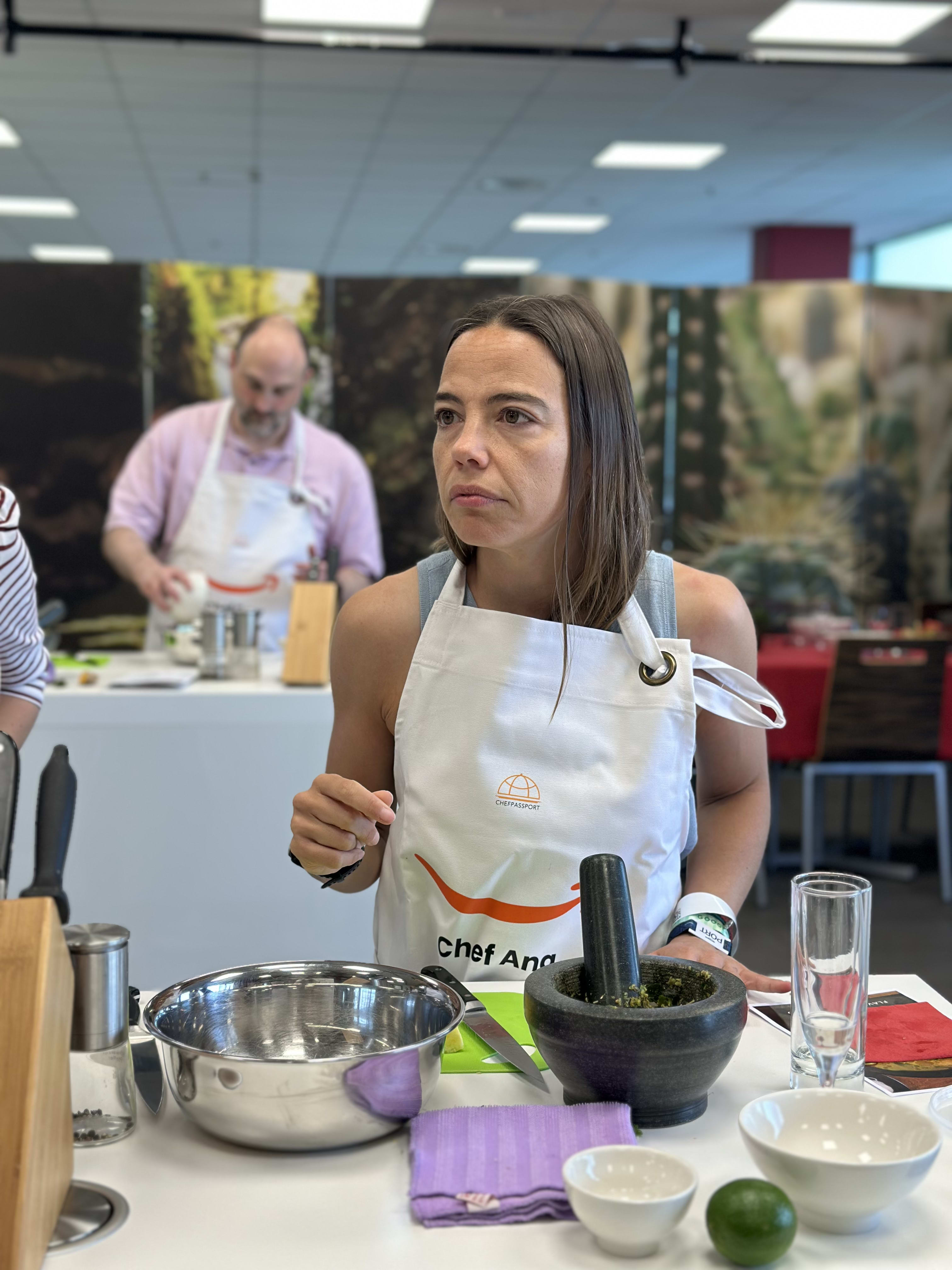 Woman in white apron using mortar and pestle during cooking class
