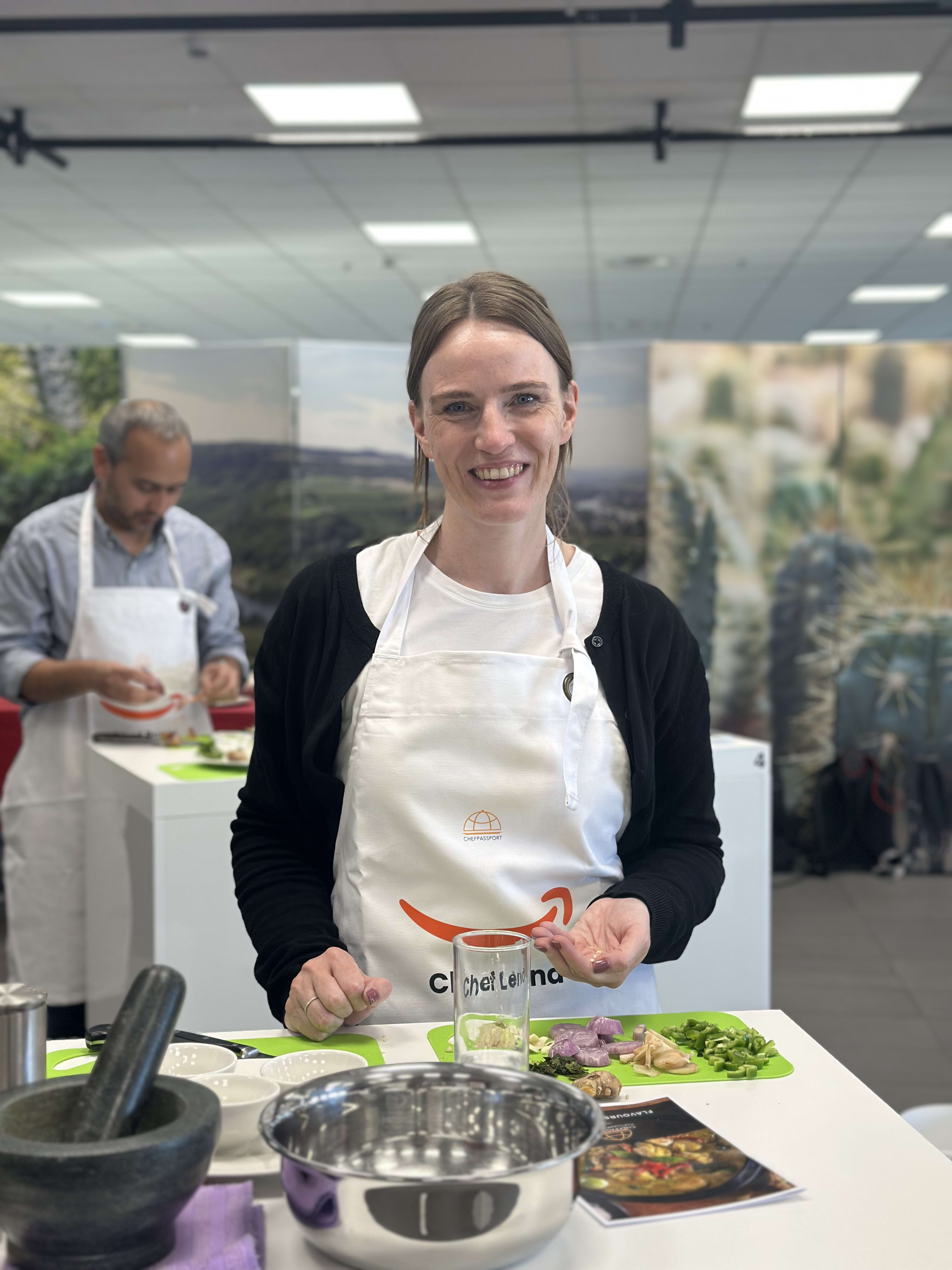 Woman in white apron smiling at cooking class with ingredients on green cutting board