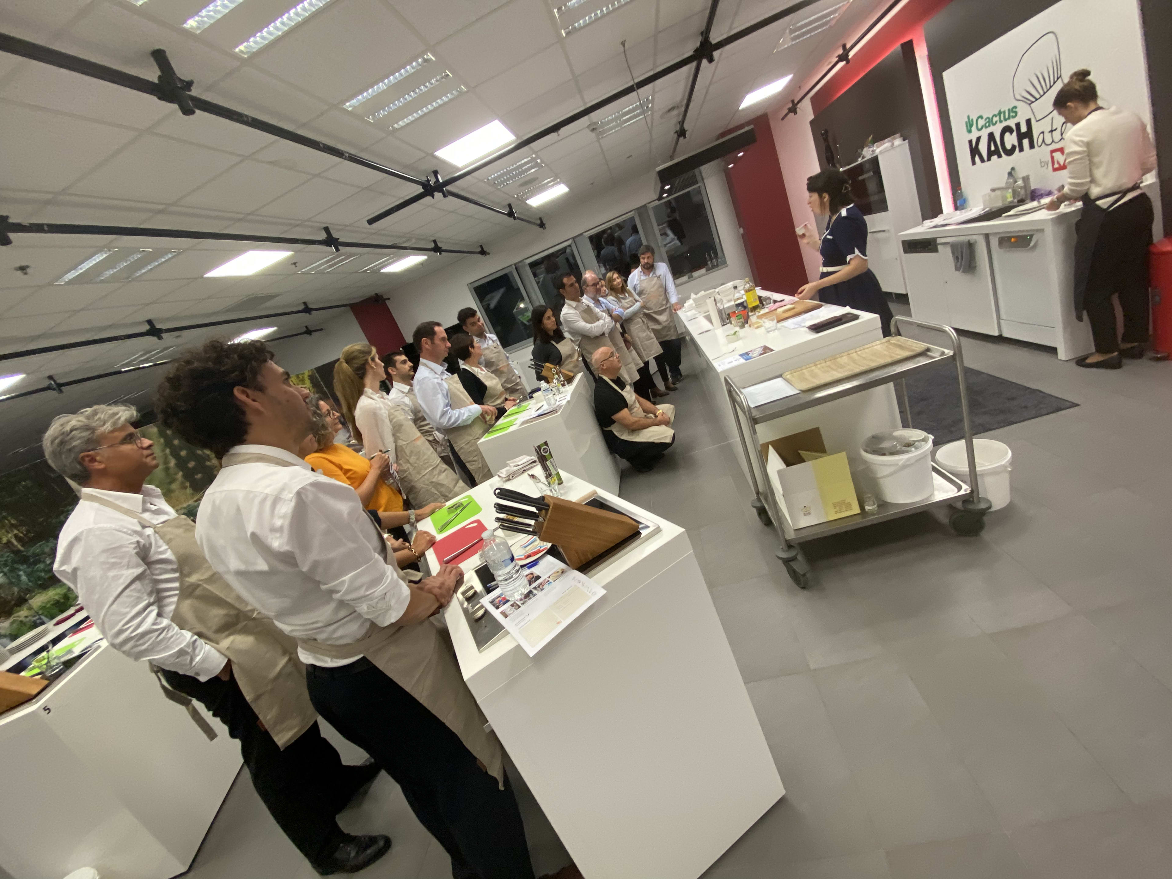 Cooking class attendees watching instructor demonstration at modern culinary school kitchen workspace