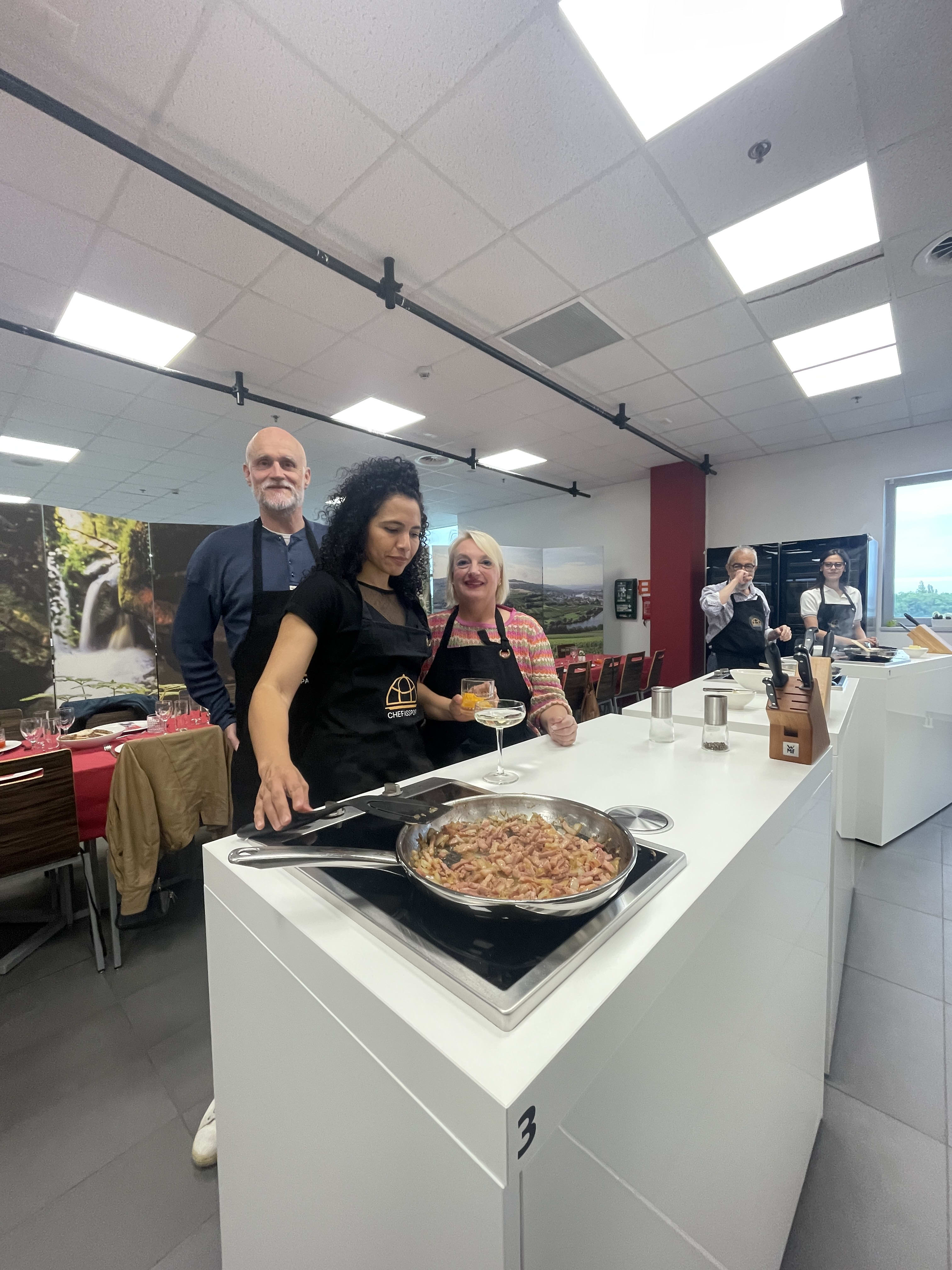 Woman cooking at stovetop station during culinary class with instructor and participants watching