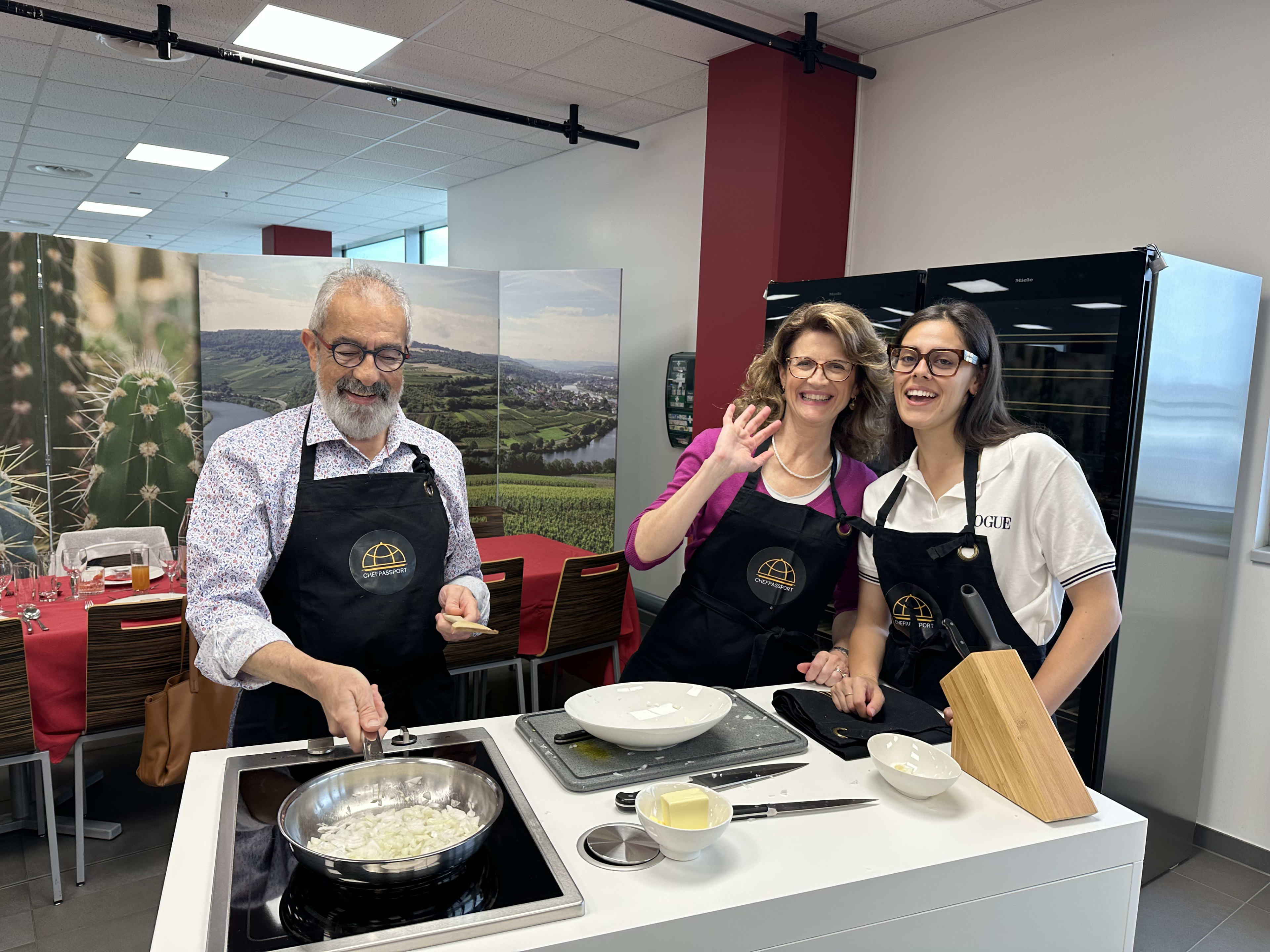 Three people in black aprons cooking together at modern kitchen station during culinary class