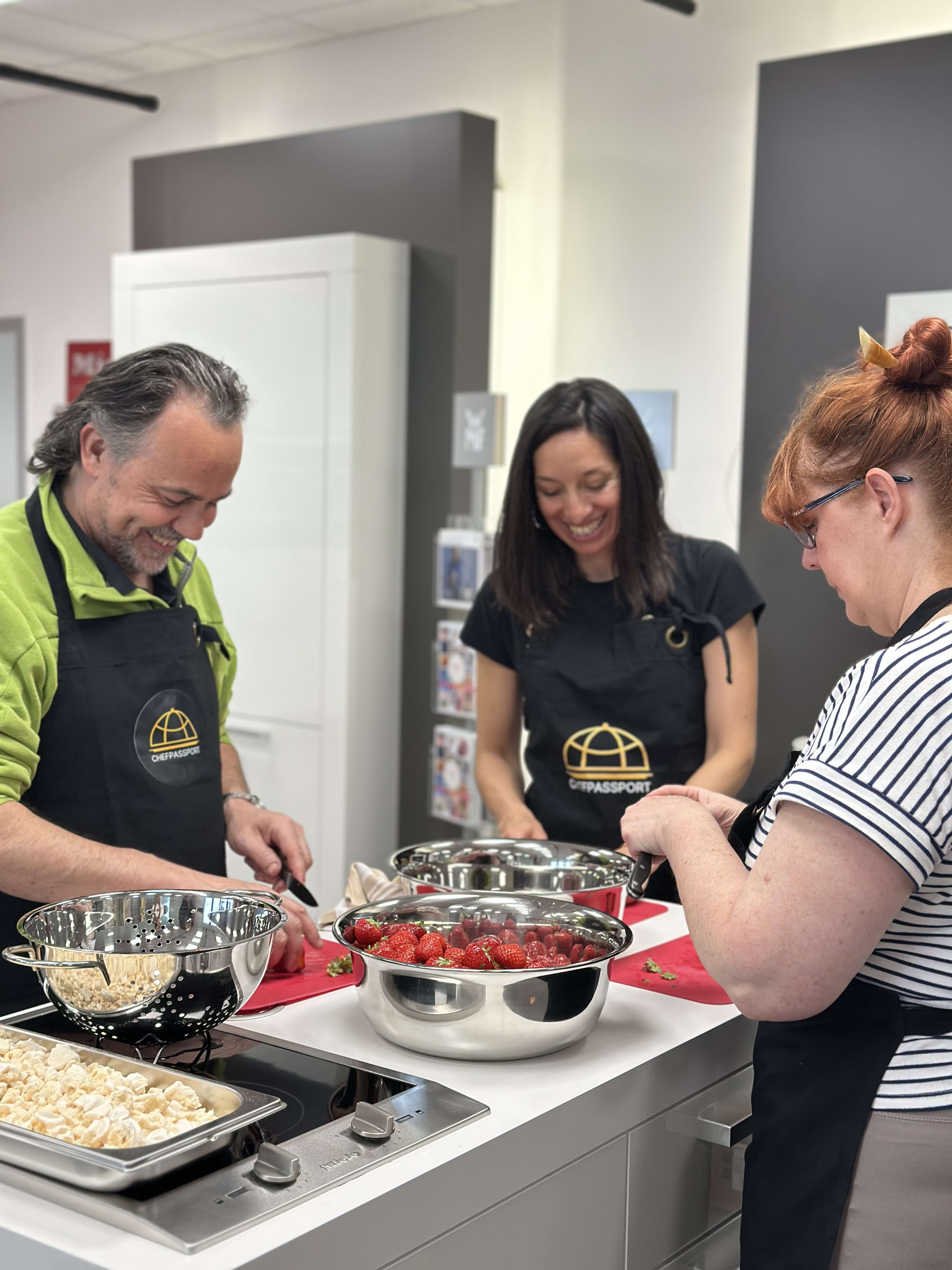Three people in CHPASSPORT aprons preparing fresh strawberries together in a modern kitchen