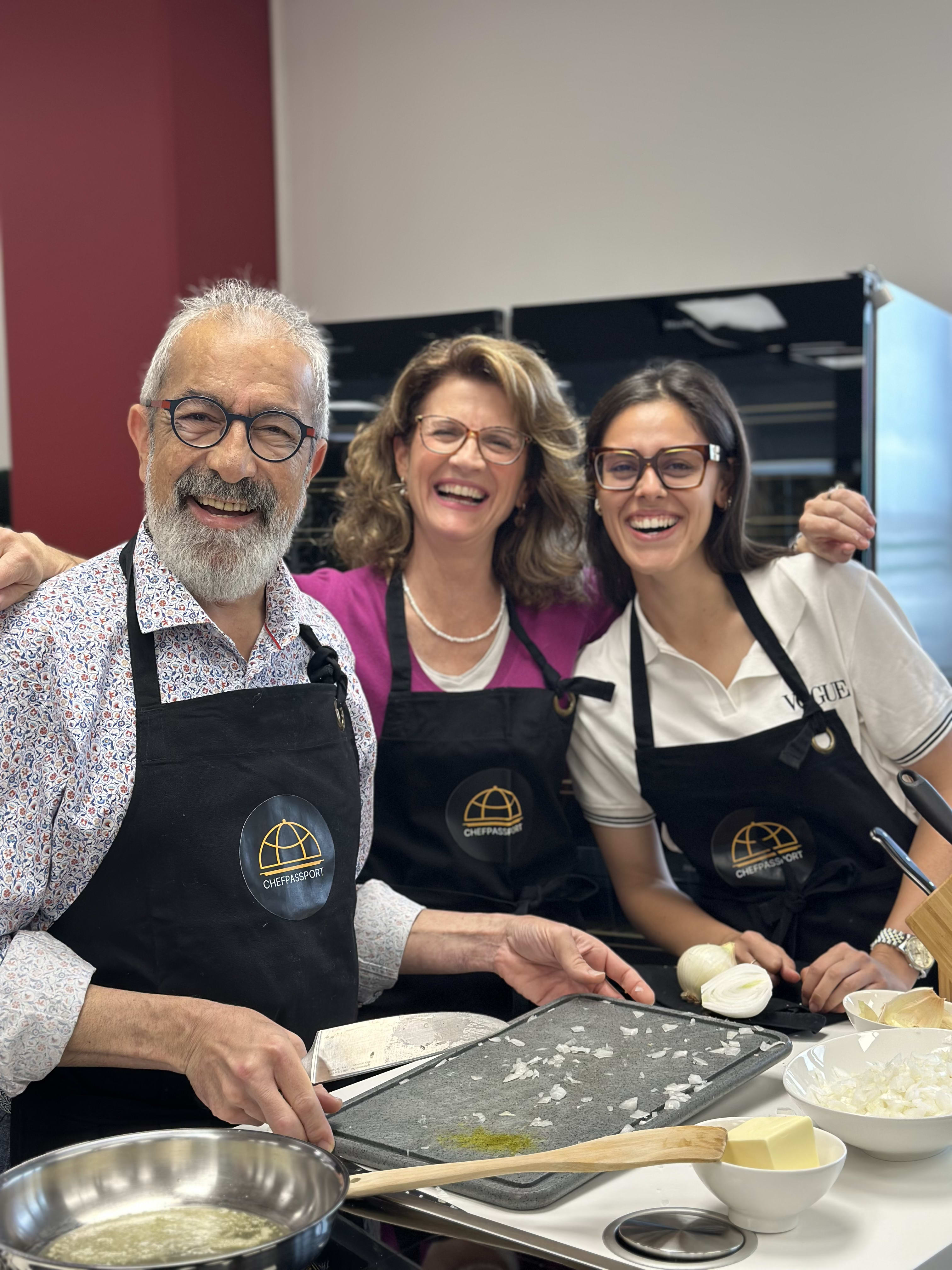 Three people wearing Chef Passport aprons smiling while preparing food in a cooking class