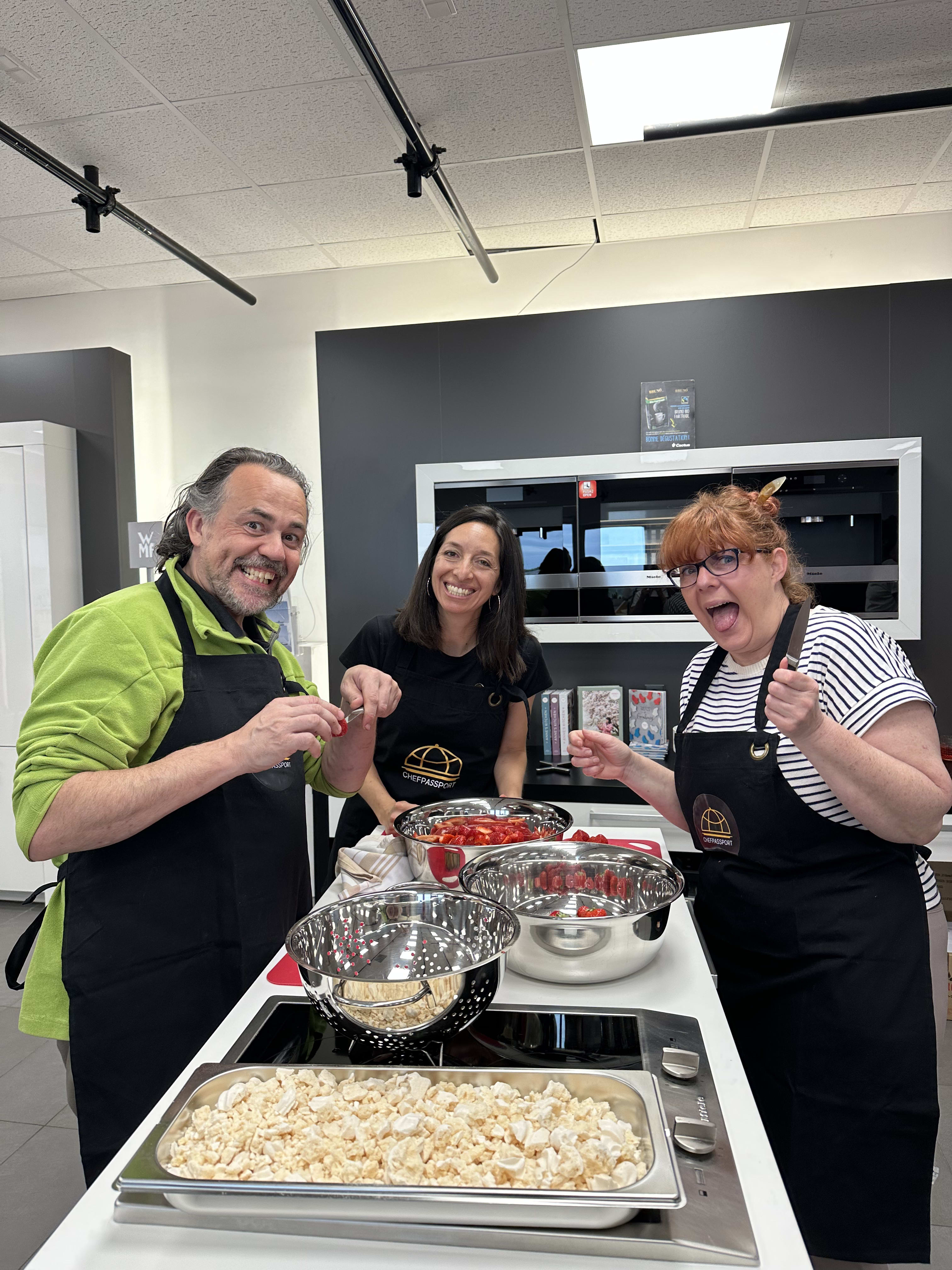 Three people in aprons preparing food with bowls and ingredients in a modern kitchen