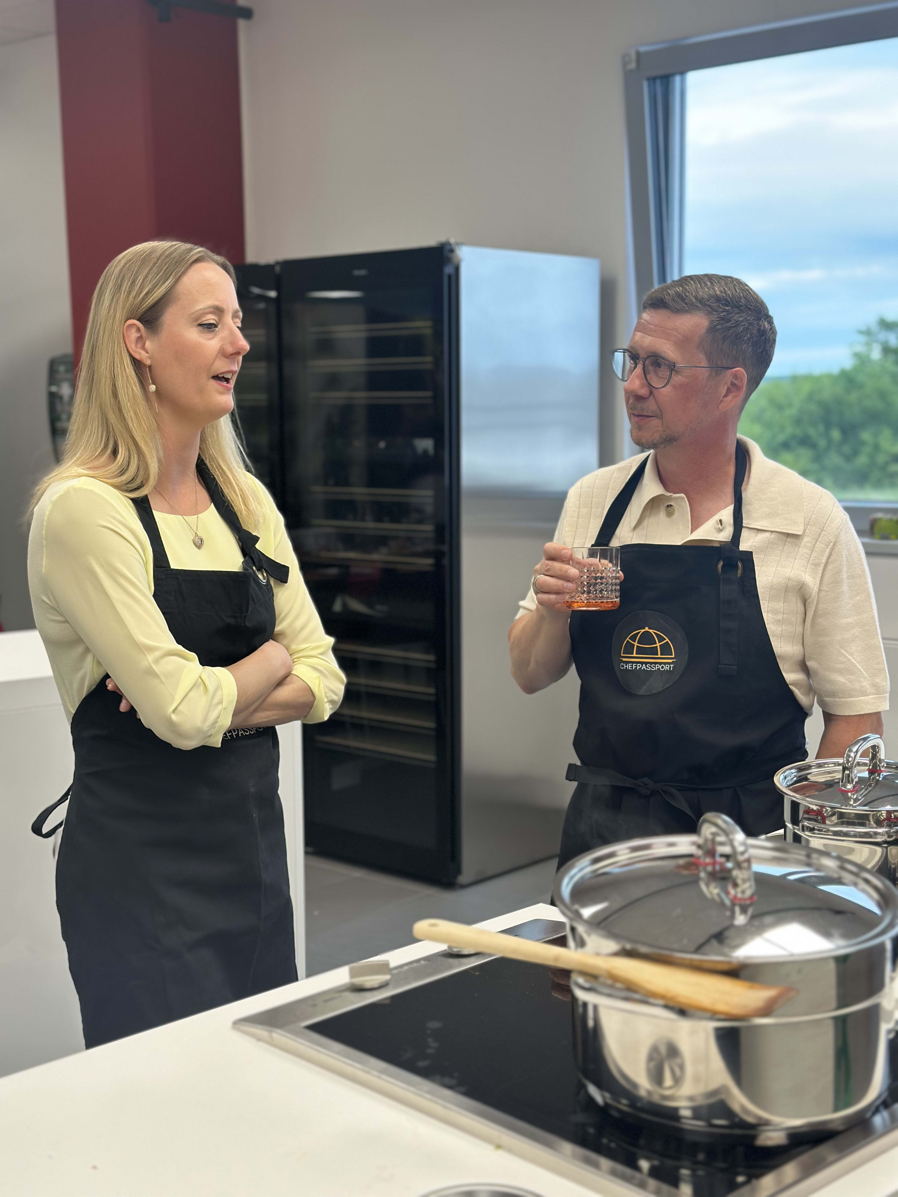 Two people in black aprons having a conversation in a modern kitchen during a cooking class
