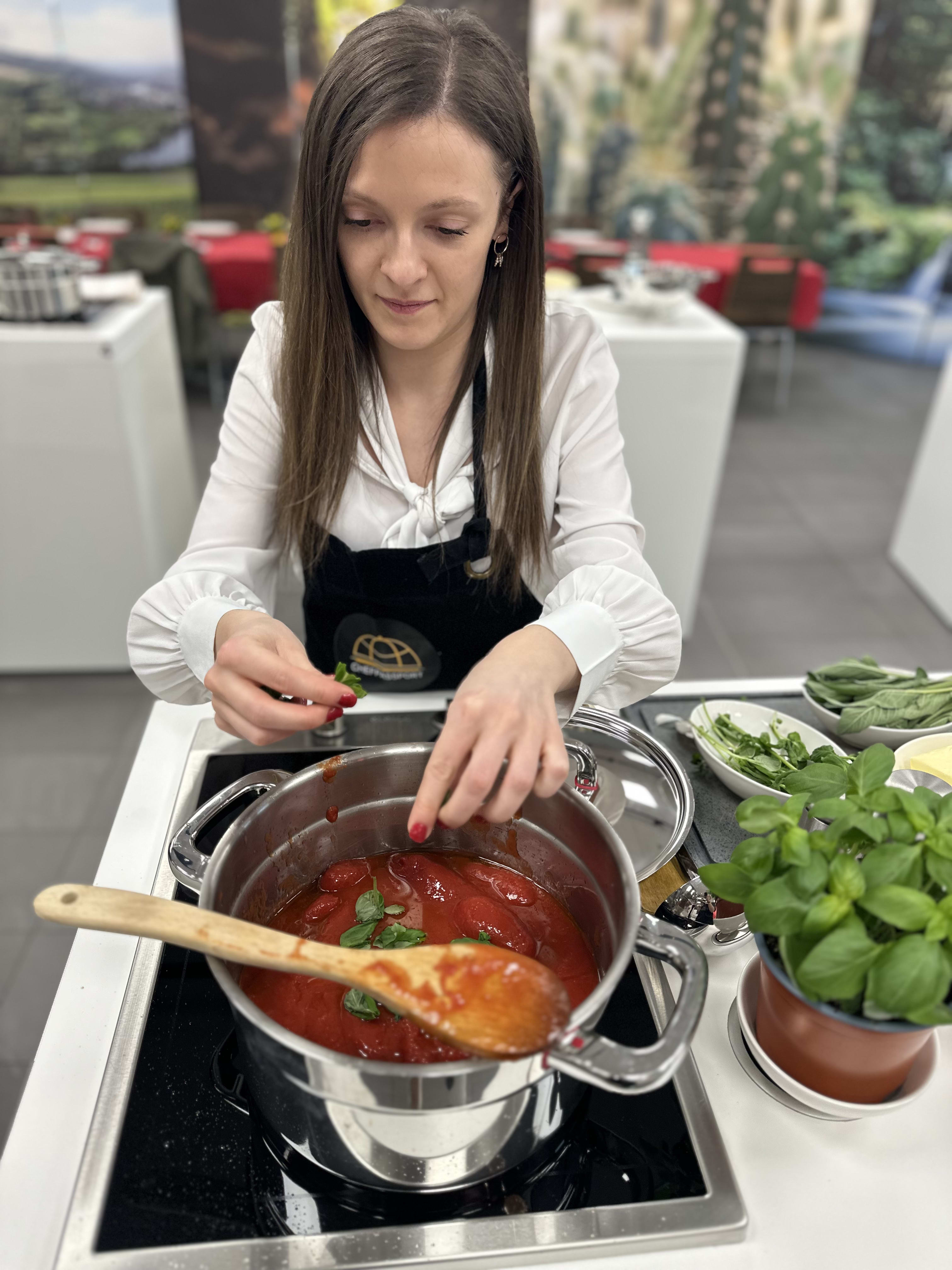 Woman in black apron stirring red tomato sauce in pot on stovetop